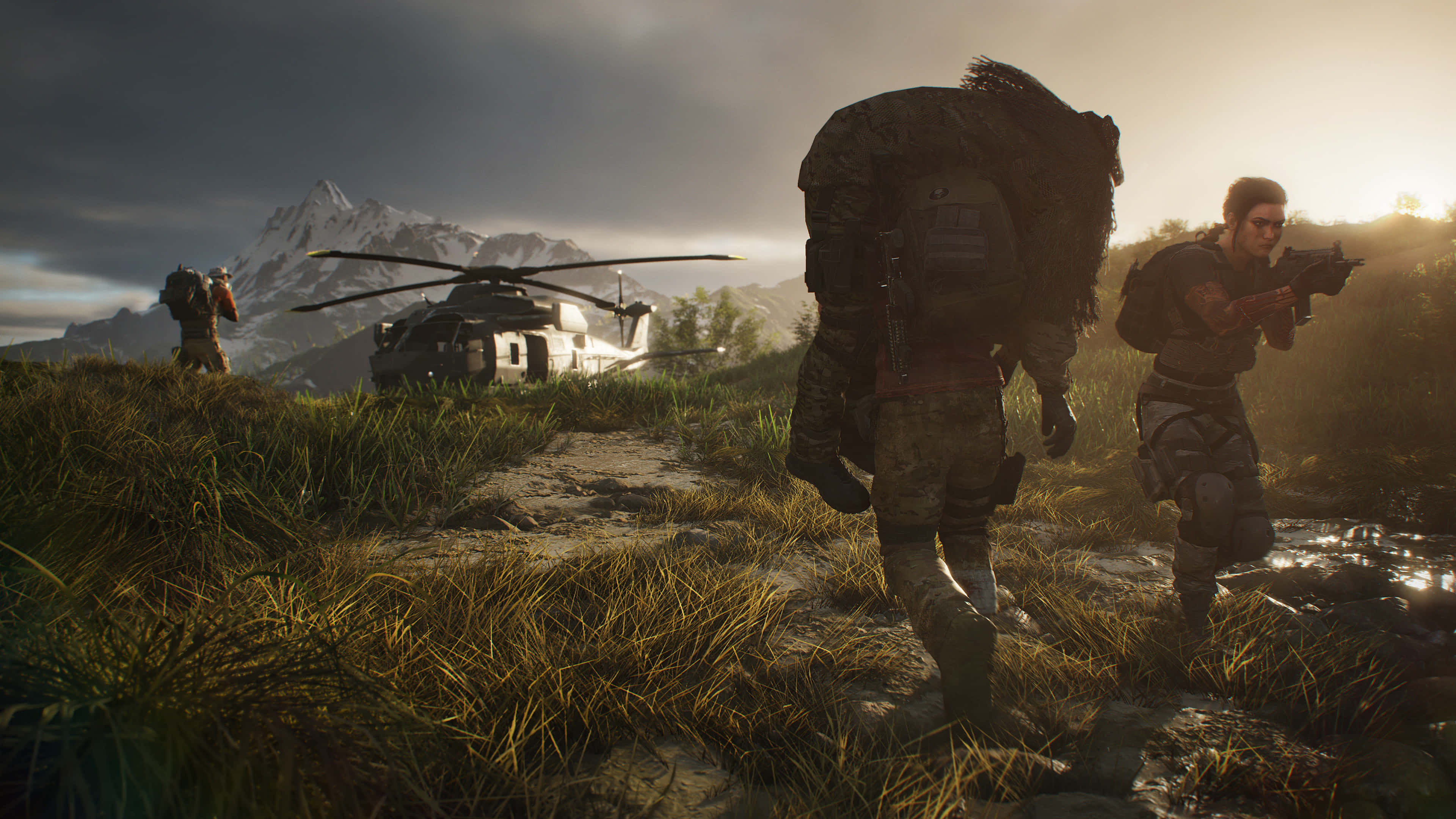 tom clancy's ghost recon wildlands 桌布 壁紙 — 身穿戰術裝備的士兵穿過泥濘的田野，走向一架墜毀的直升機，背景中白雪覆蓋的山峰在戲劇性的日落天空下聳立。