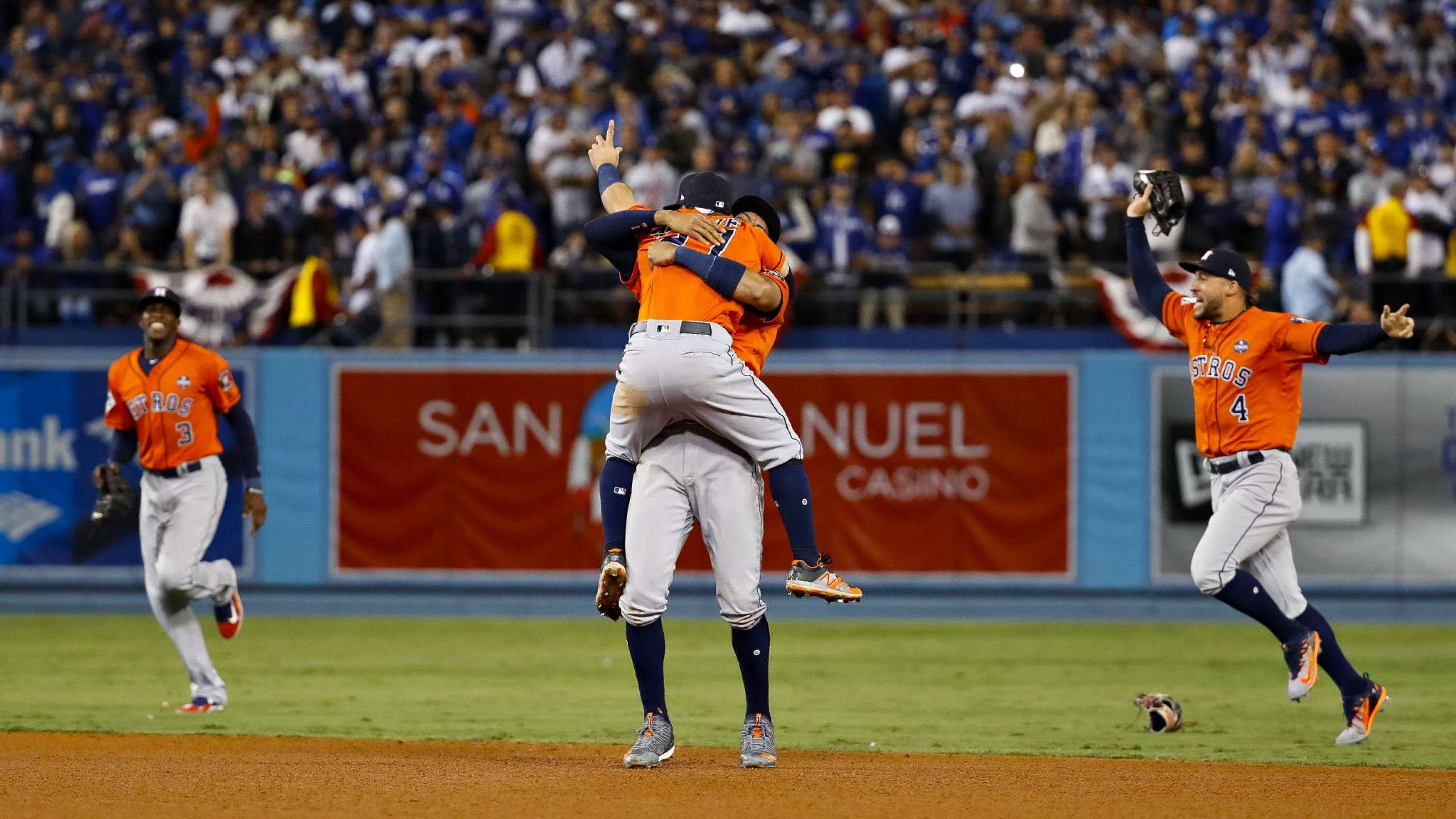 Astros 桌布 壁紙 — 身穿橙色球衣的棒球運動員在體育場燈光下擁抱並高舉手臂慶祝勝利。