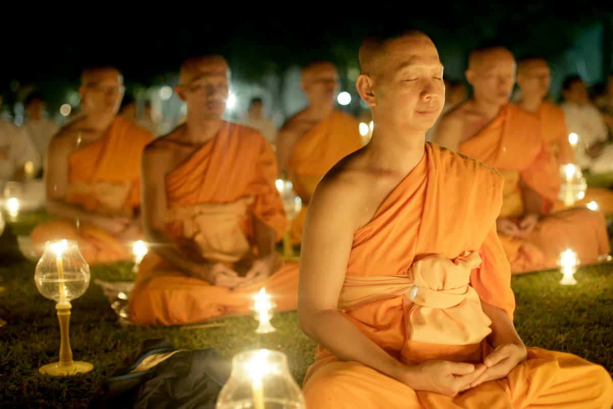 religion 桌布 壁紙 — 身穿橙色長袍的僧侶在夜間於草地上被發光的蠟燭包圍，平靜地冥想。