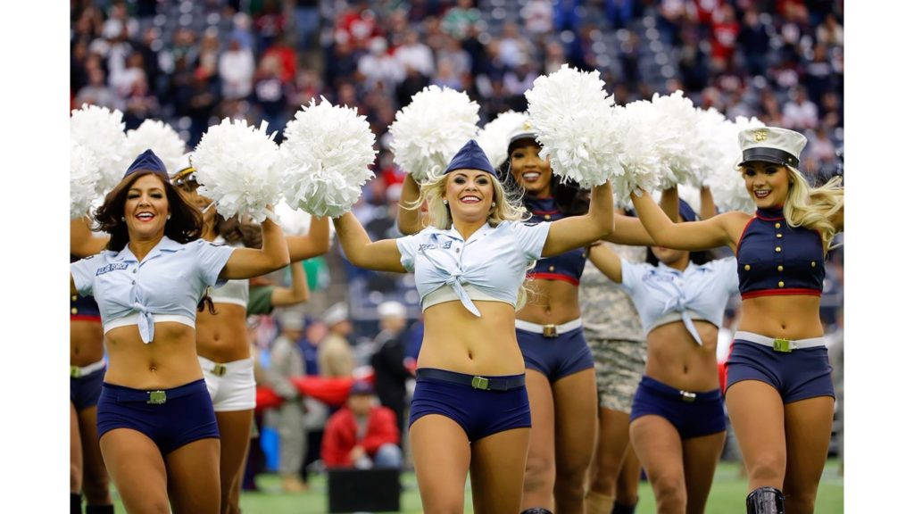 Cheerleader 桌布 壁紙 — 身穿海軍藍和白色制服的啦啦隊員在足球場上，在人群面前用彩球表演。