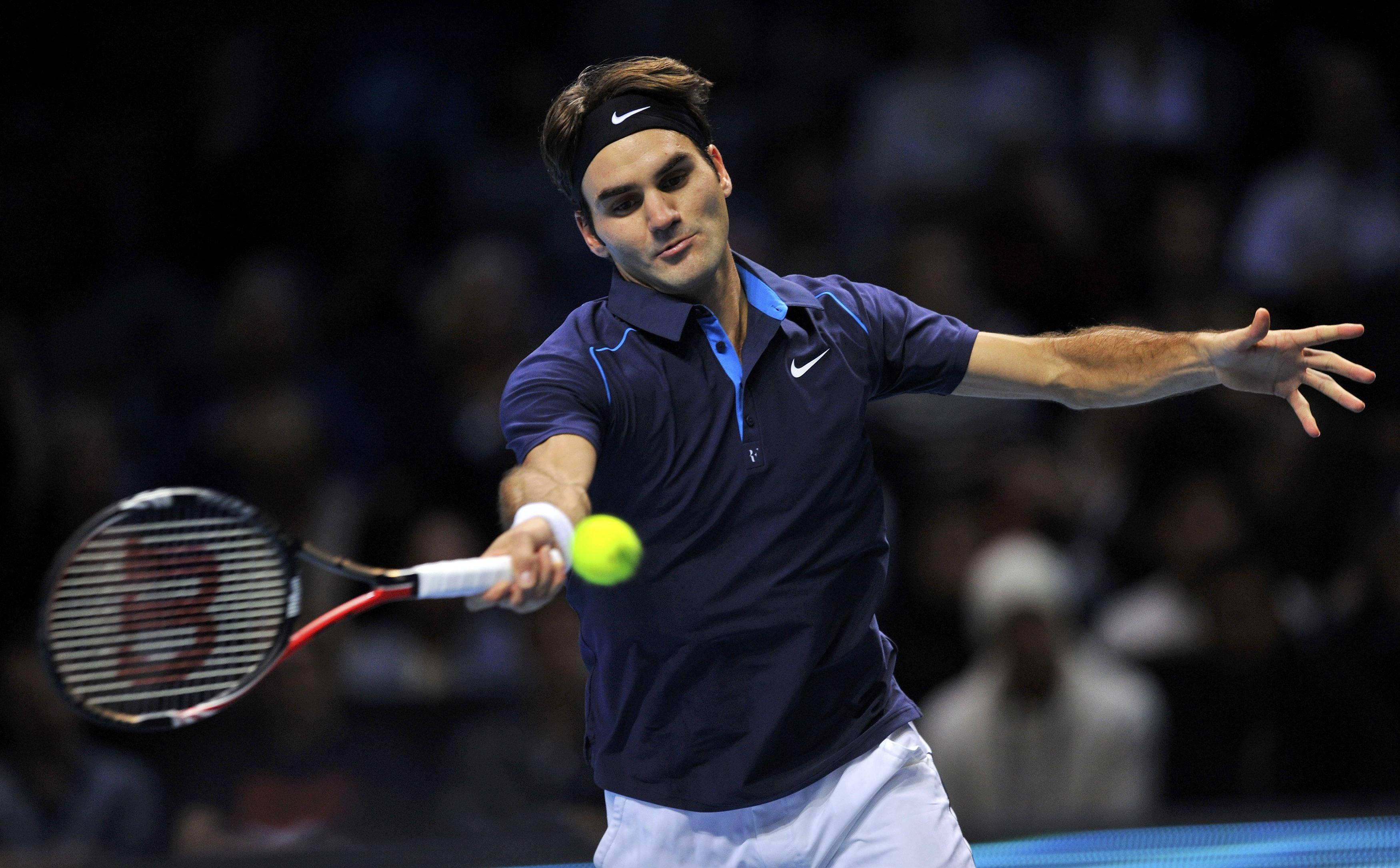 roger 桌布 壁紙 — 身穿海軍藍襯衫的網球選手在比賽中專注地揮拍擊打亮黃色的球。