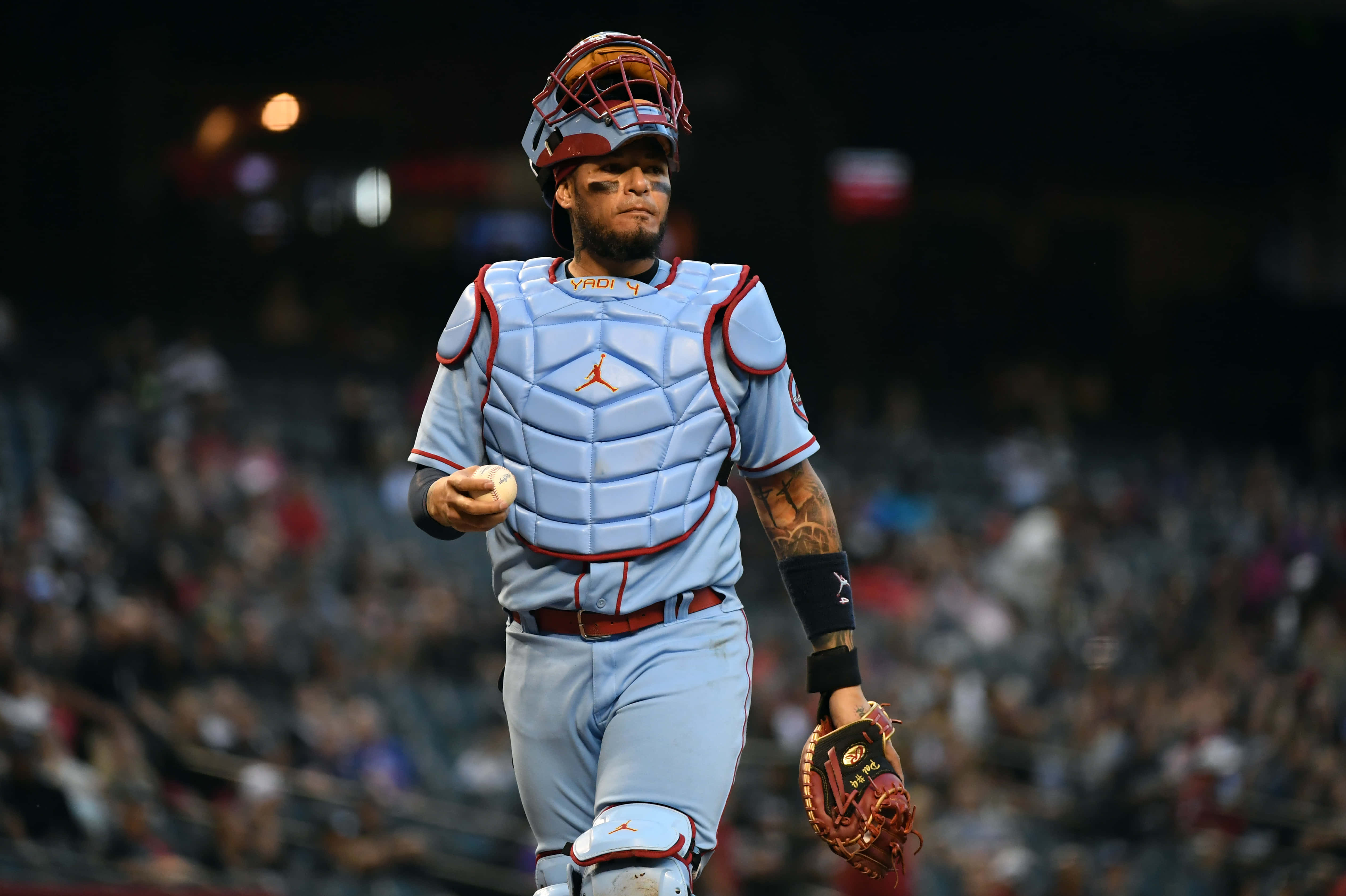 Yadier Molina 桌布 壁紙 — 身穿淺藍色裝備的棒球捕手自信地走過球場燈光，手持球和手套。