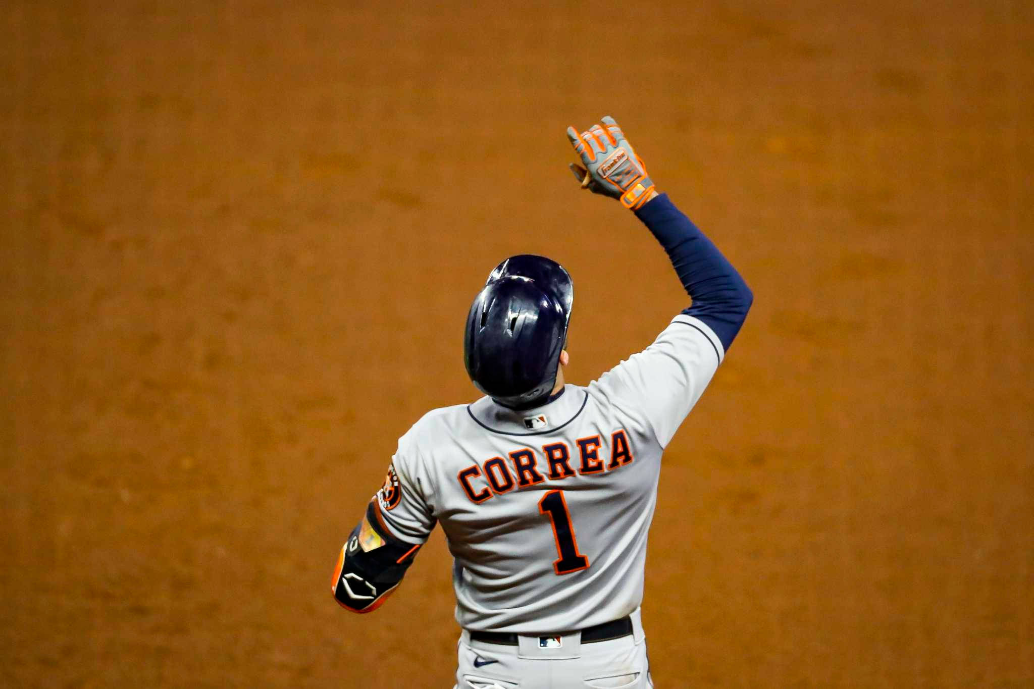 Carlos Correa 桌布 壁紙 — 身穿灰色球衣的棒球選手Correa在球場燈光下於泥地場上高舉手套慶祝勝利。