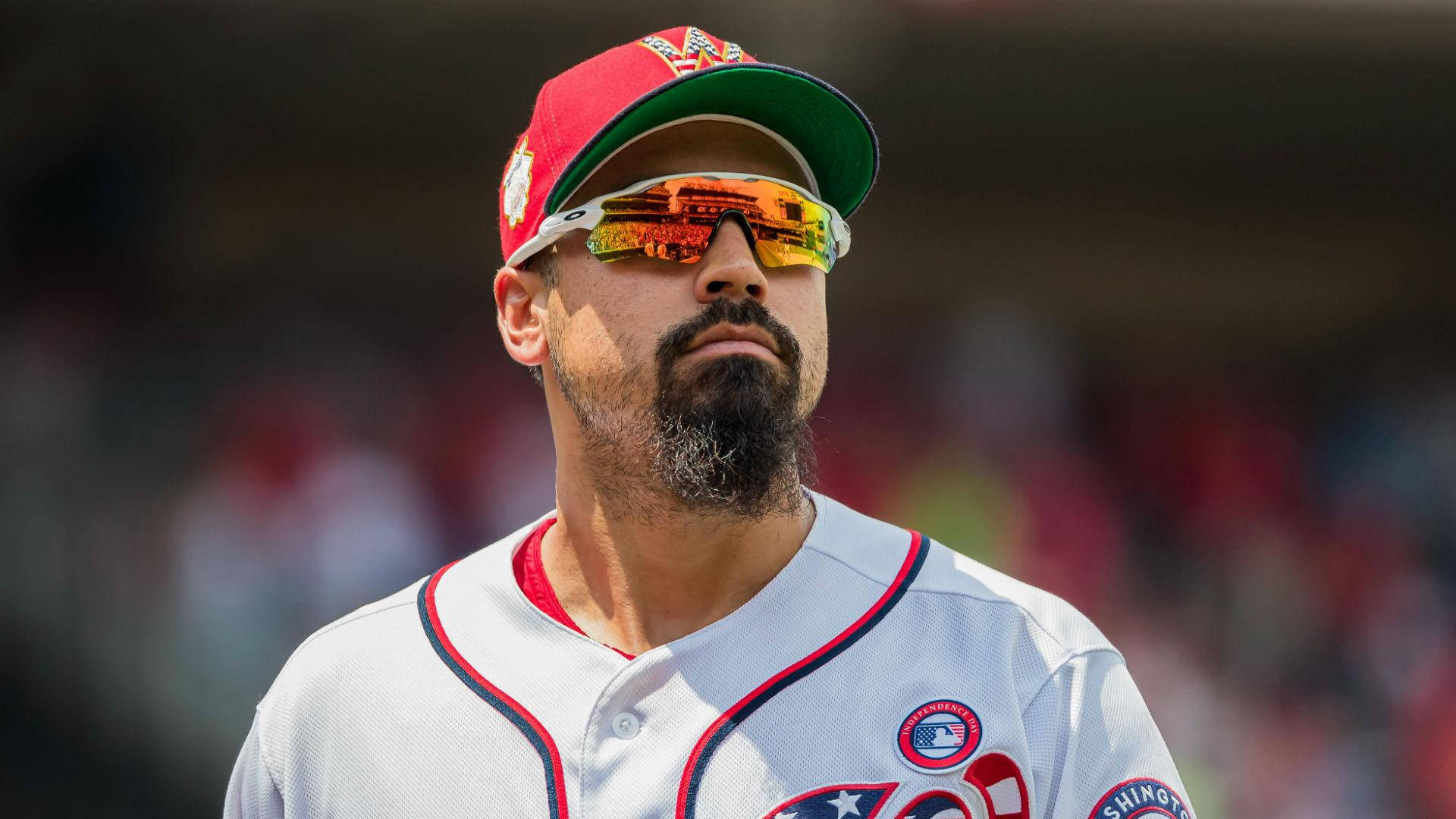 anthony rendon 桌布 壁紙 — 身穿白色制服和紅色帽子的棒球運動員在明亮的日光下戴著反光太陽眼鏡專注地凝視。