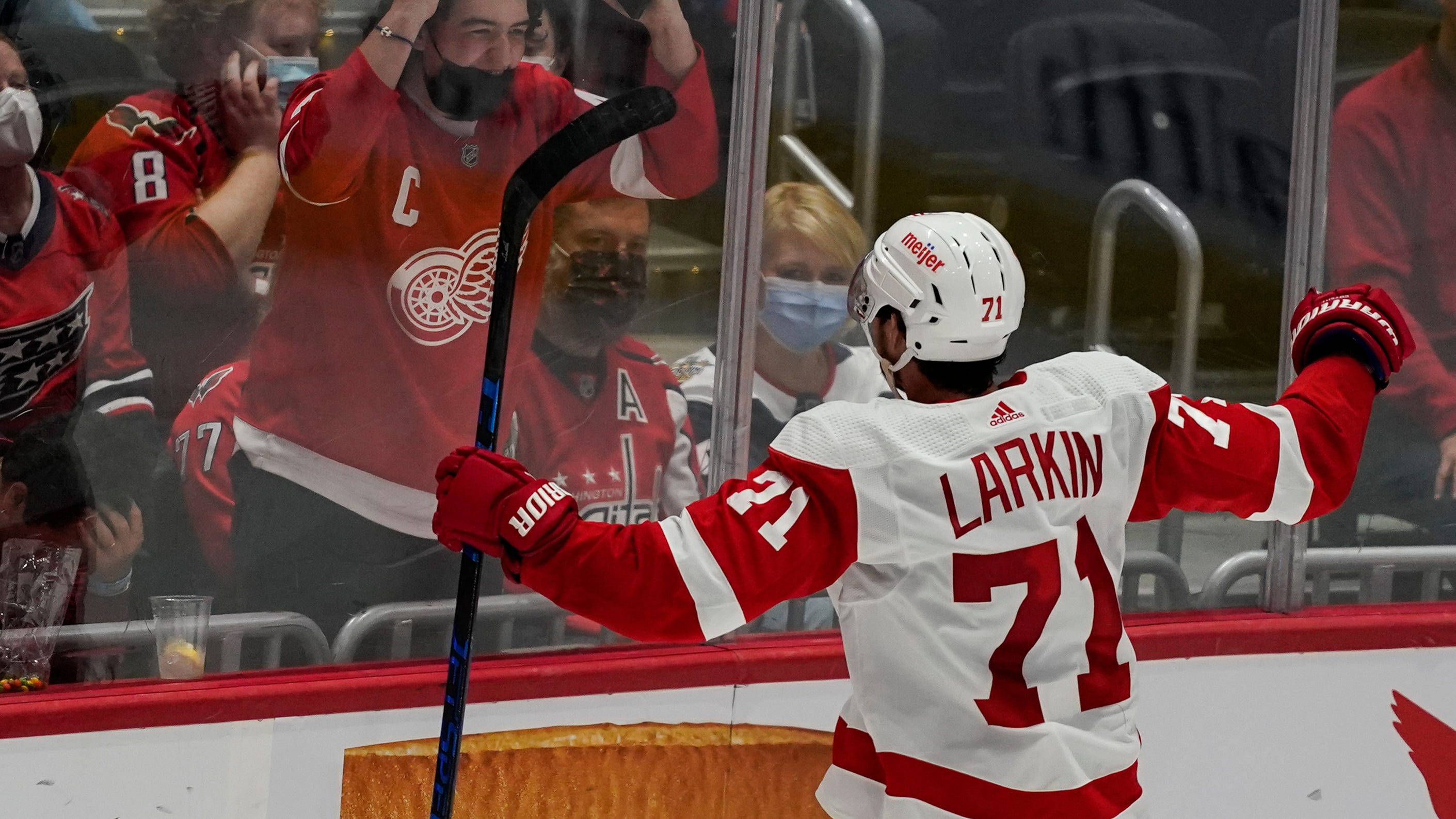 hockey 桌布 壁紙 — 身穿白色和紅色球衣的冰球運動員Larkin高舉雙臂慶祝，紅色球衣的球迷在玻璃後歡呼。
