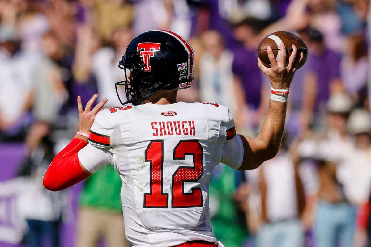 Texas Tech 桌布 壁紙 — 身穿白色和紅色球衣的四分衛Shough在白天比賽中準備投擲橄欖球，背景是模糊的紫色人群。