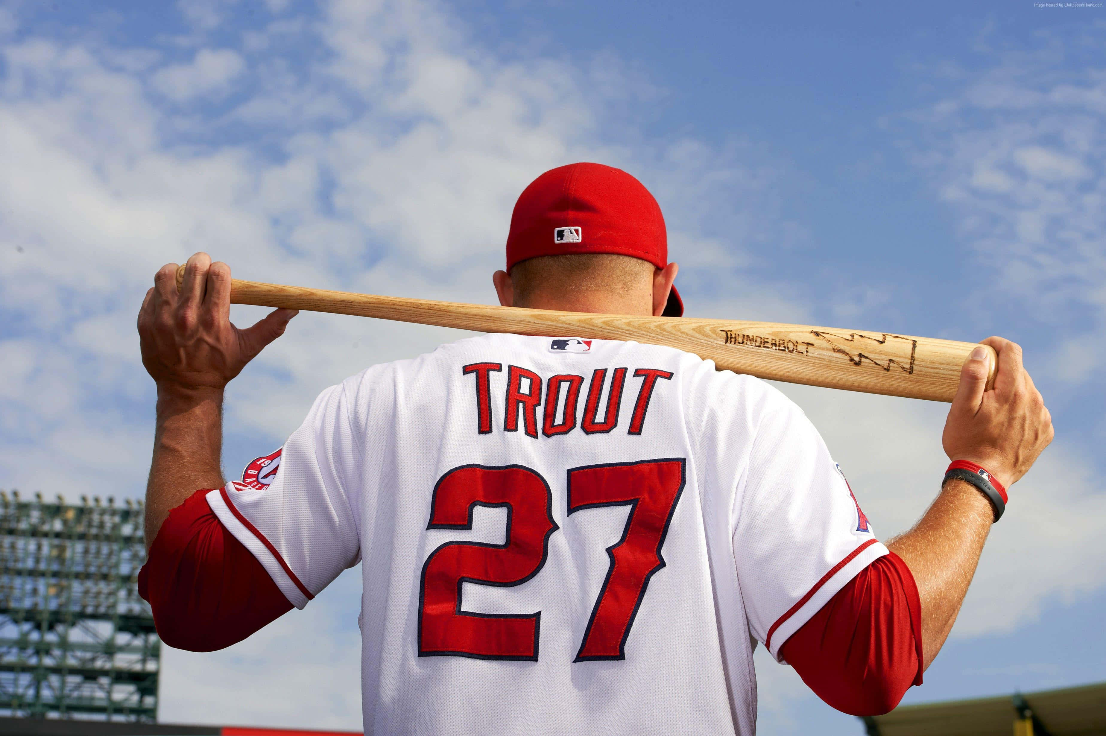 MLB Players 桌布 壁紙 — 身穿白色和紅色球衣的棒球運動員Mike Trout在明亮的藍天和零星雲朵背景下將球棒扛在肩上。