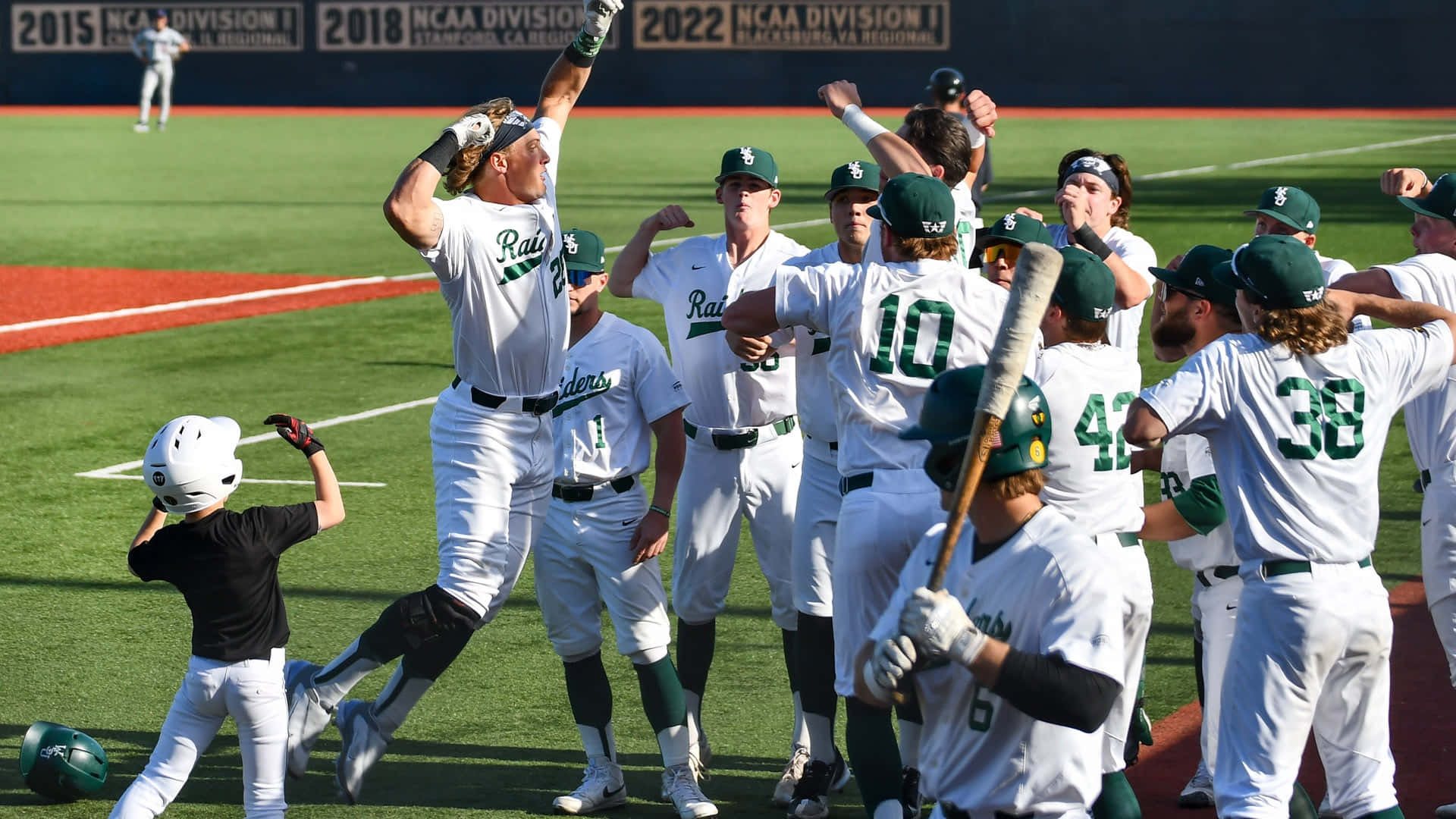 College Baseball 桌布 壁紙 — 身穿白色和綠色球衣的棒球運動員在陽光明媚的球場上與年輕的吉祥物一起慶祝勝利。