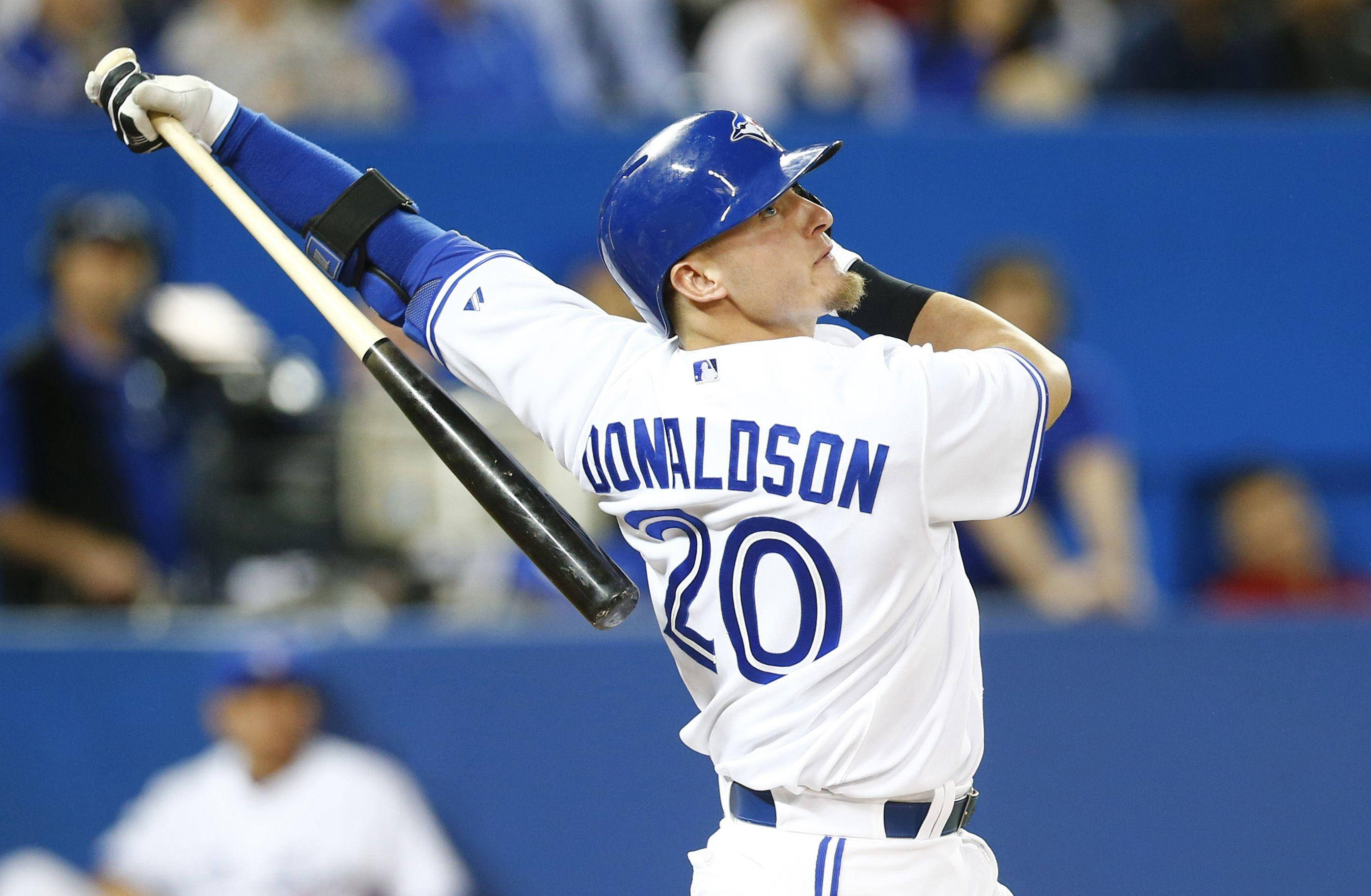 MLB 桌布 壁紙 — 身穿白色和藍色球衣的棒球選手Donaldson在夜間比賽中，在球場燈光下全神貫注地揮棒。