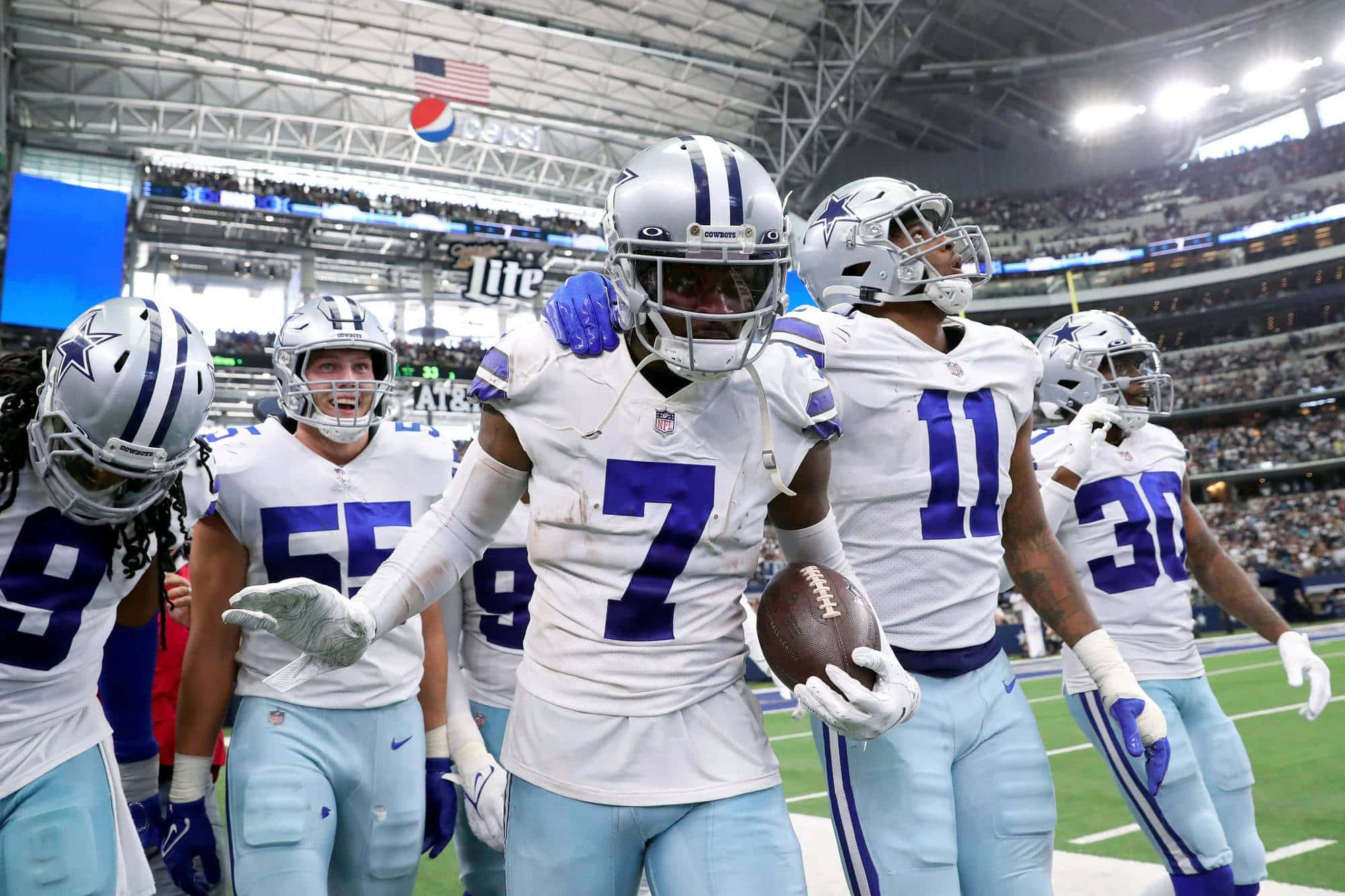 Dallas Cowboys Players 桌布 壁紙 — 身穿白色和藍色球衣的達拉斯牛仔隊美式足球員在球場燈光下慶祝。