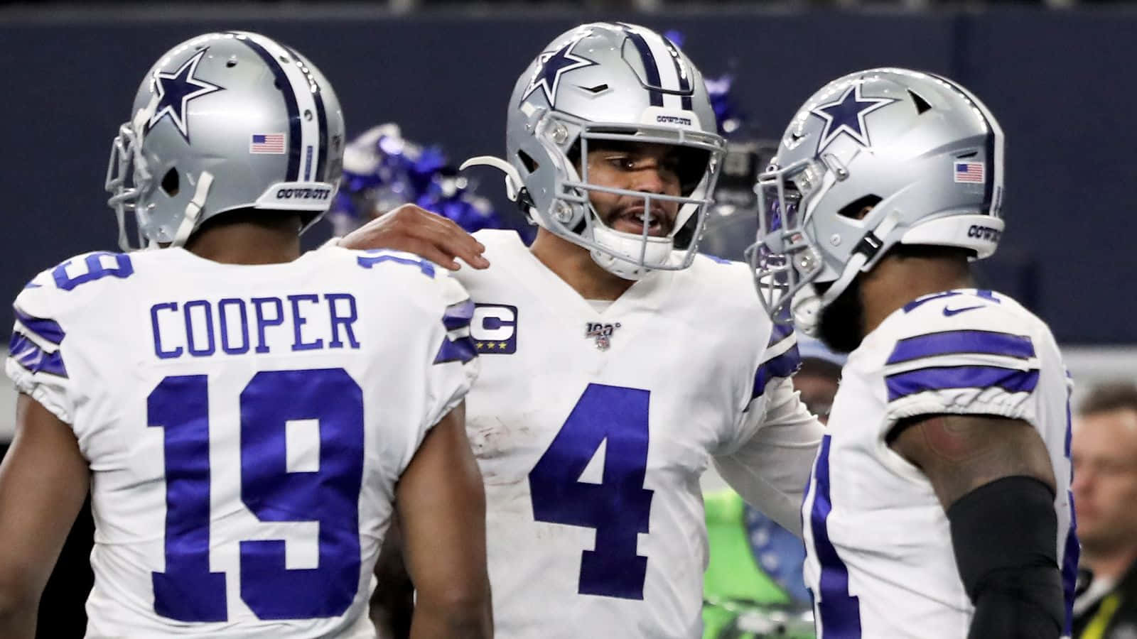 Dallas Cowboys Players 桌布 壁紙 — 身穿白色和藍色球衣的達拉斯牛仔隊美式足球員在比賽期間於球場上聚集。