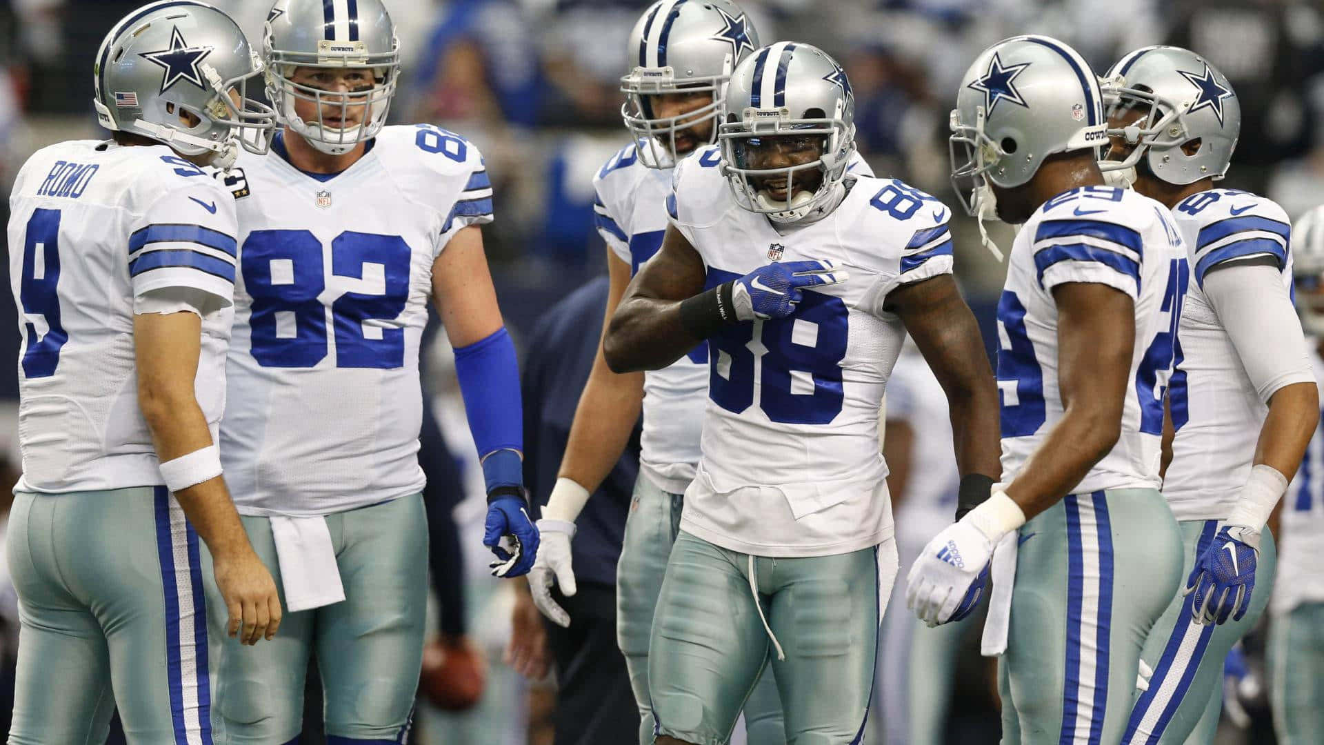 Dallas Cowboys Players 桌布 壁紙 — 身穿白色和藍色球衣的達拉斯牛仔隊美式足球員在比賽期間於場上聚集。