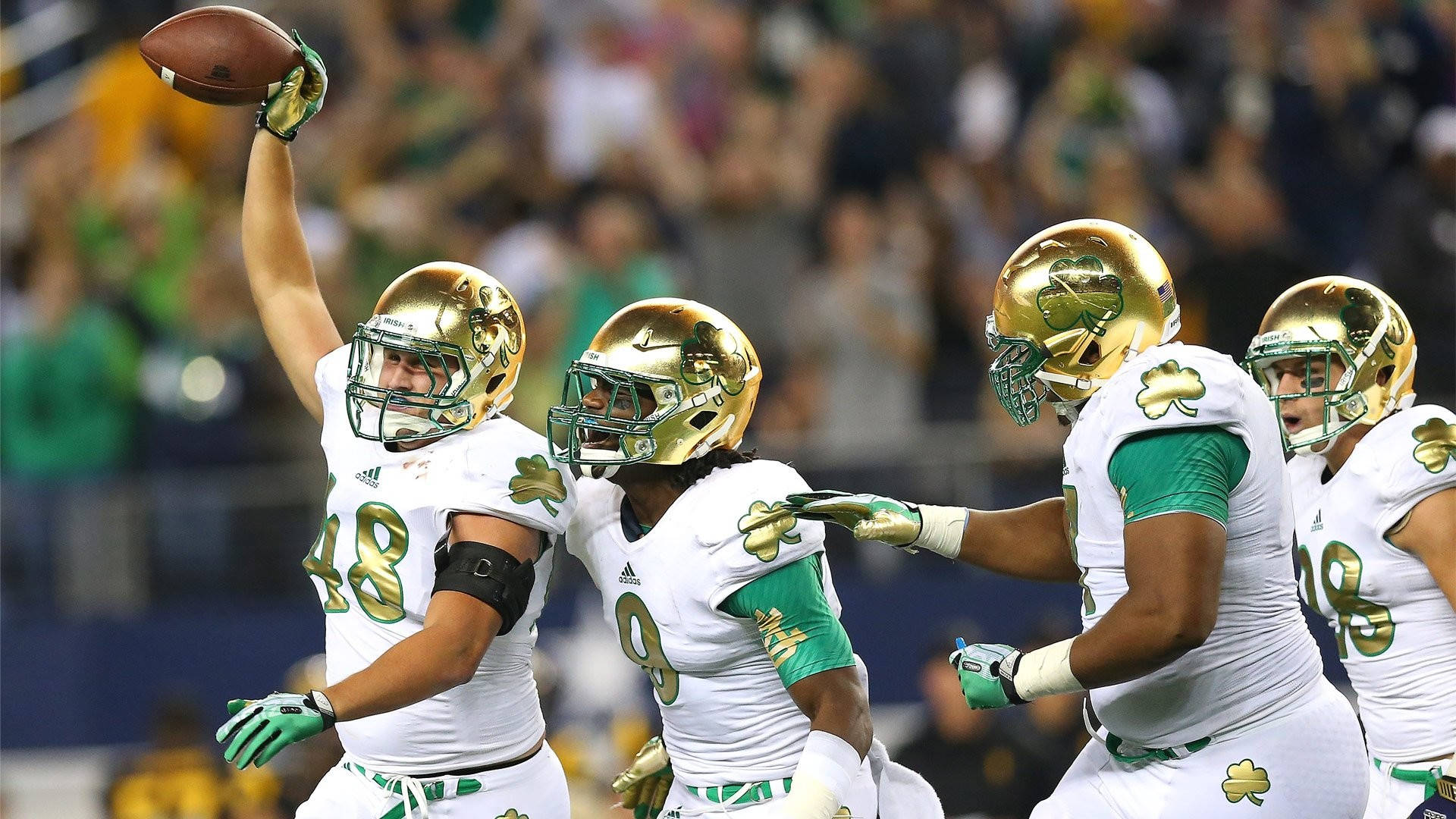 Notre Dame Football 桌布 壁紙 — 身穿白色和金色球衣的足球員慶祝達陣，其中一名球員高舉球，勝利的姿態。