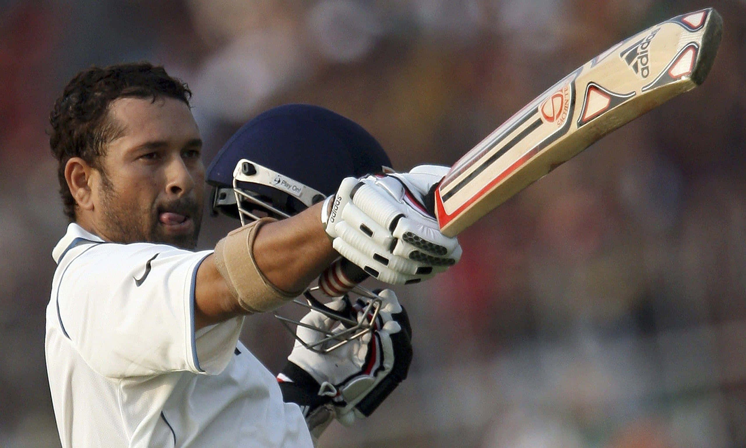 Sachin Tendulkar 桌布 壁紙 — 身穿白色球衣的板球運動員在球場燈光下專注地揮動球棒。