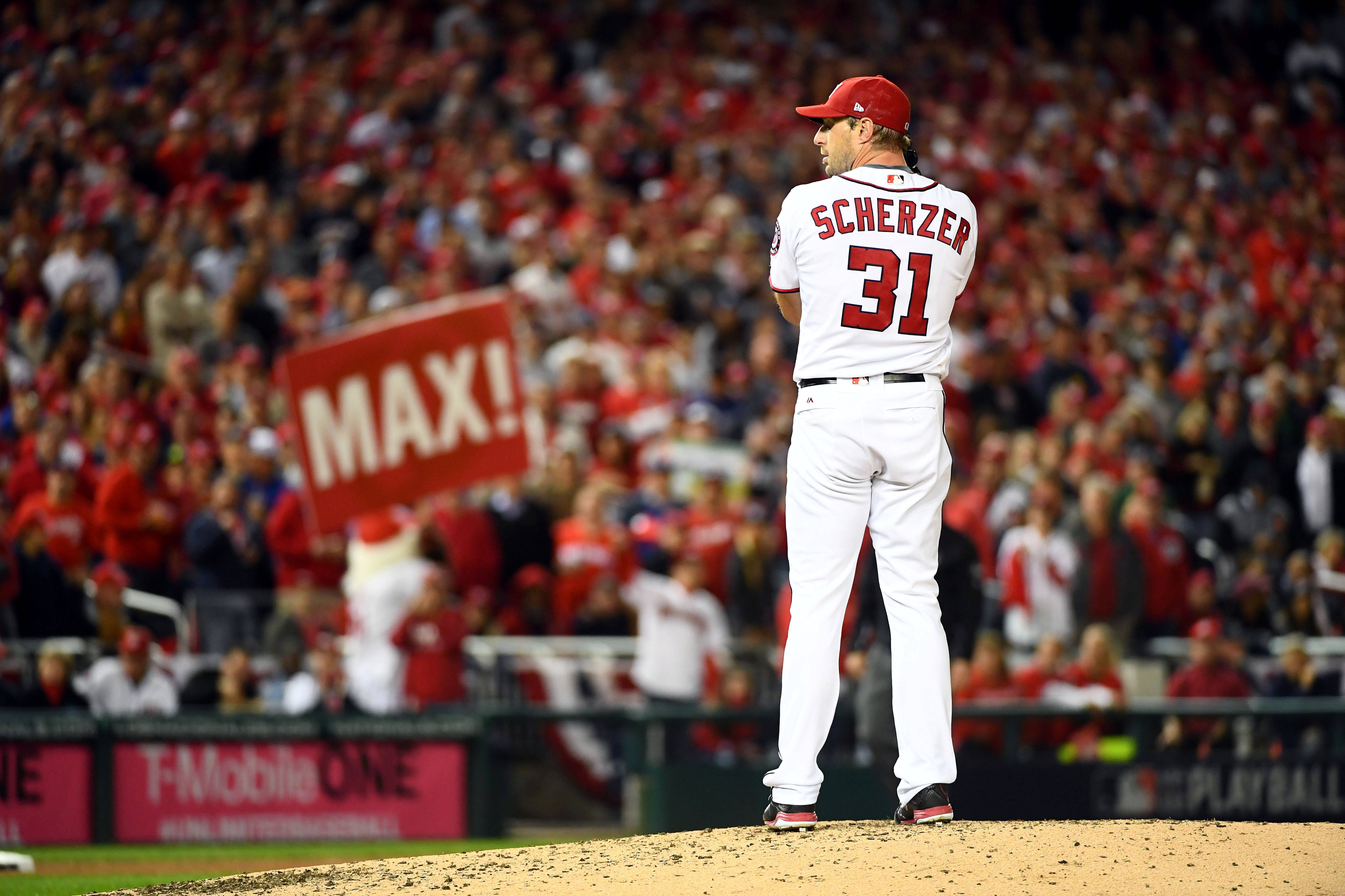 Max Scherzer 桌布 壁紙 — 身穿白色球衣的棒球投手Scherzer在夜間球場燈光下站在投手丘上面對人群。