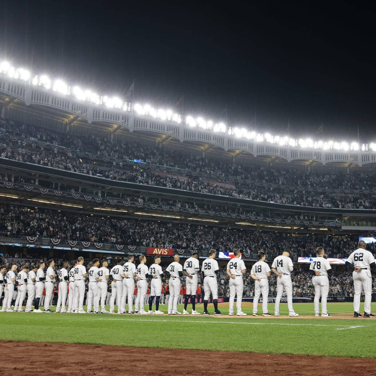 Stadium 桌布 壁紙 — 身穿白色球衣的棒球運動員在夜間明亮的球場燈光下，站在綠色球場上排成一排，身後是坐滿觀眾的看台。