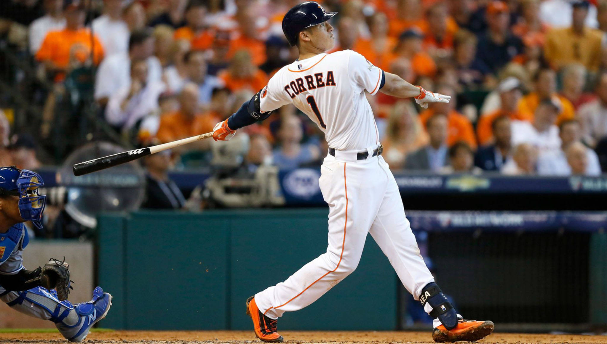 Carlos Correa 桌布 壁紙 — 身穿白色球衣的棒球選手Correa在球場燈光下揮棒，捕手蹲在本壘板後方。