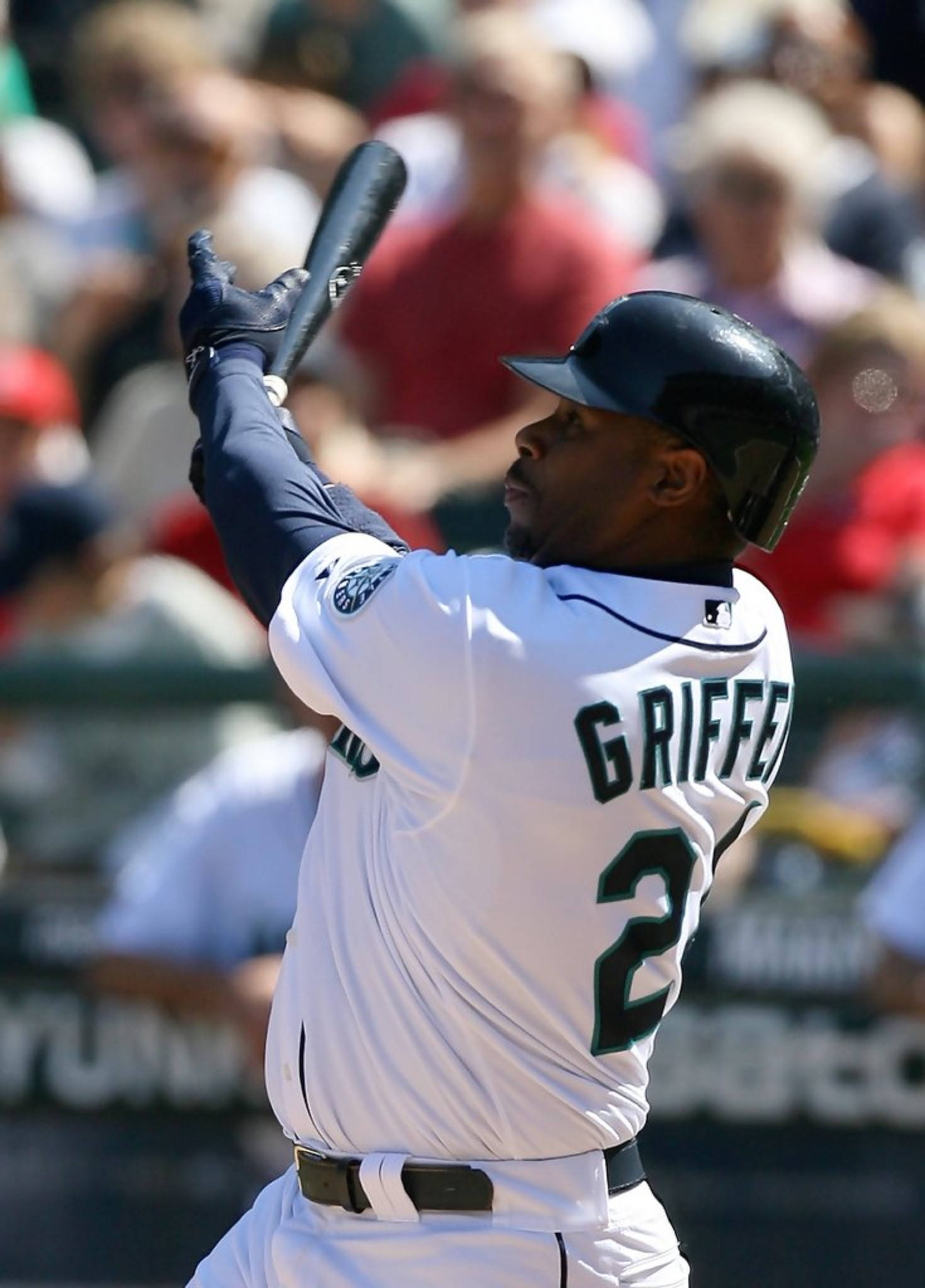 ken 桌布 壁紙 — 身穿白色球衣的棒球選手Griffey Jr.在揮棒中途揮動球棒，背景有模糊的人群。