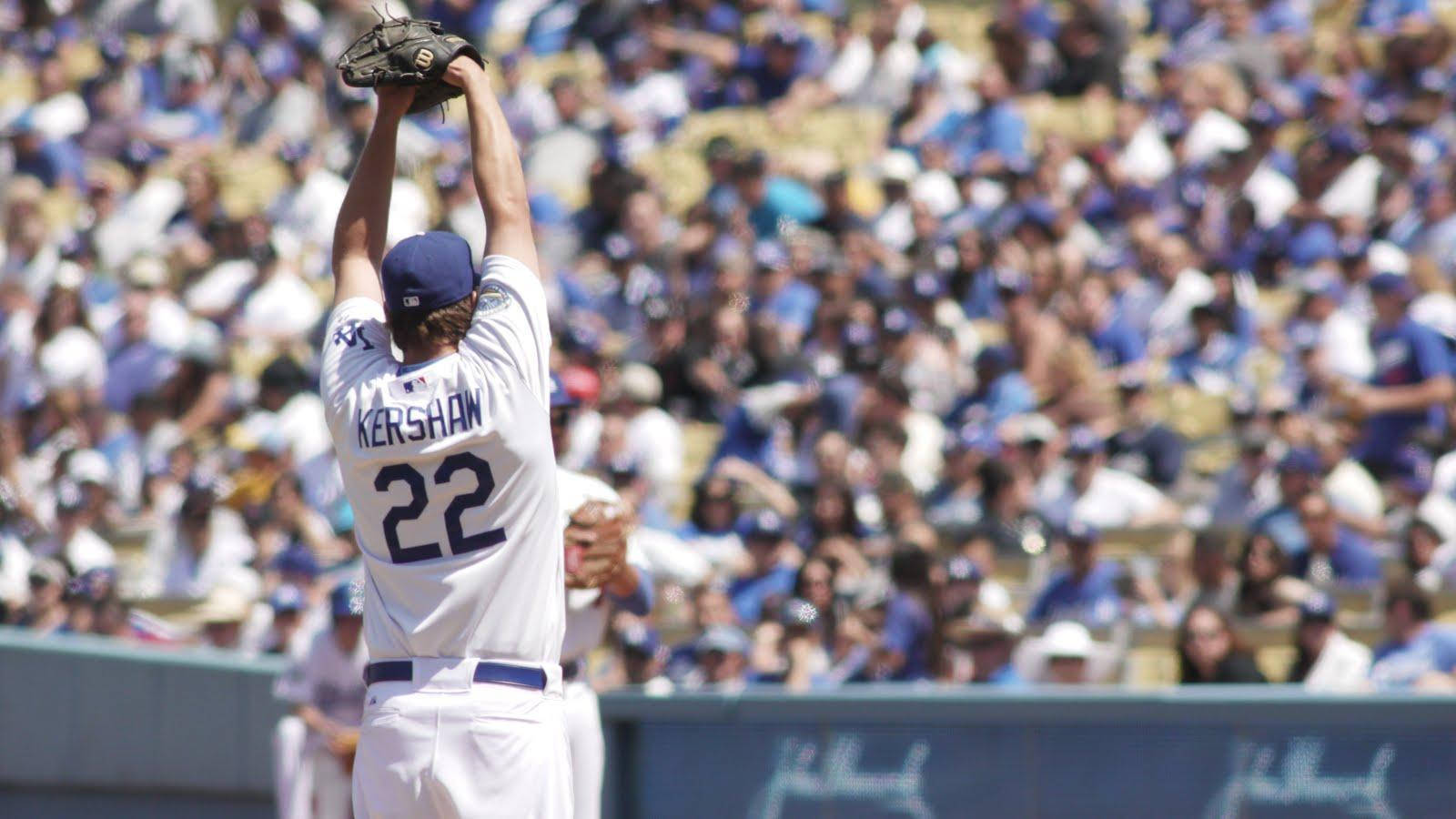 MLB 桌布 壁紙 — 身穿白色球衣的棒球選手Kershaw（22號）在陽光明媚的球場上，在歡呼的群眾面前，高舉戴著手套的雙手，慶祝勝利。