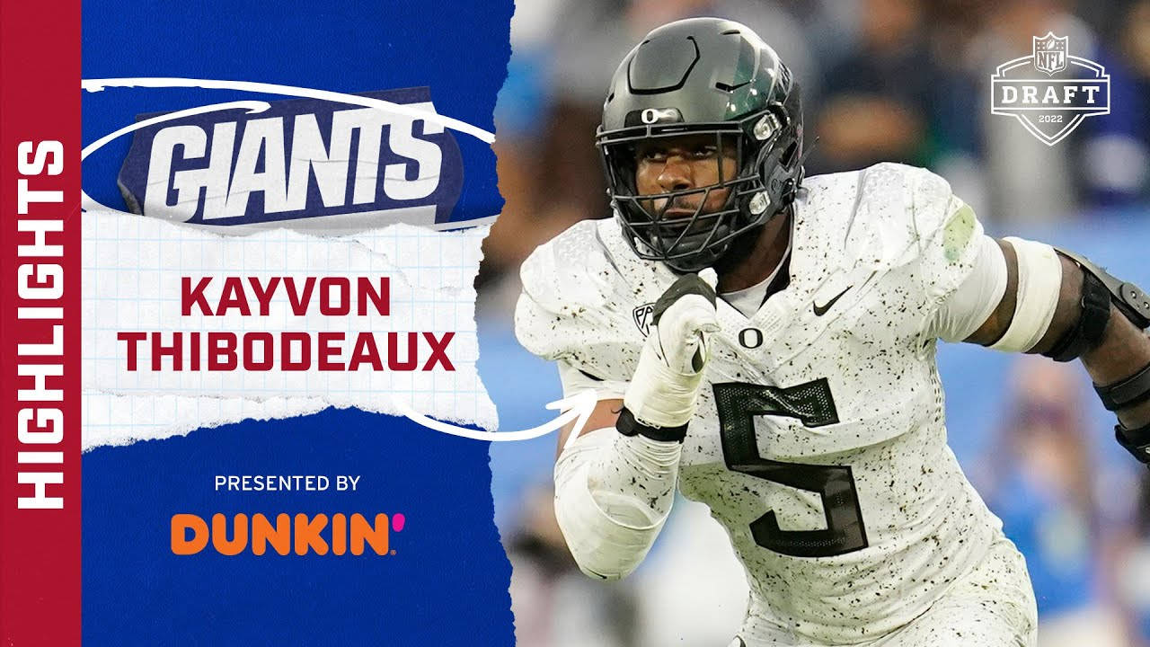 運動 桌布 壁紙 — 身穿白色球衣的足球運動員 Kayvon Thibodeaux 戴著頭盔，在帶有巨人隊品牌的藍色圖形背景前動態衝刺。