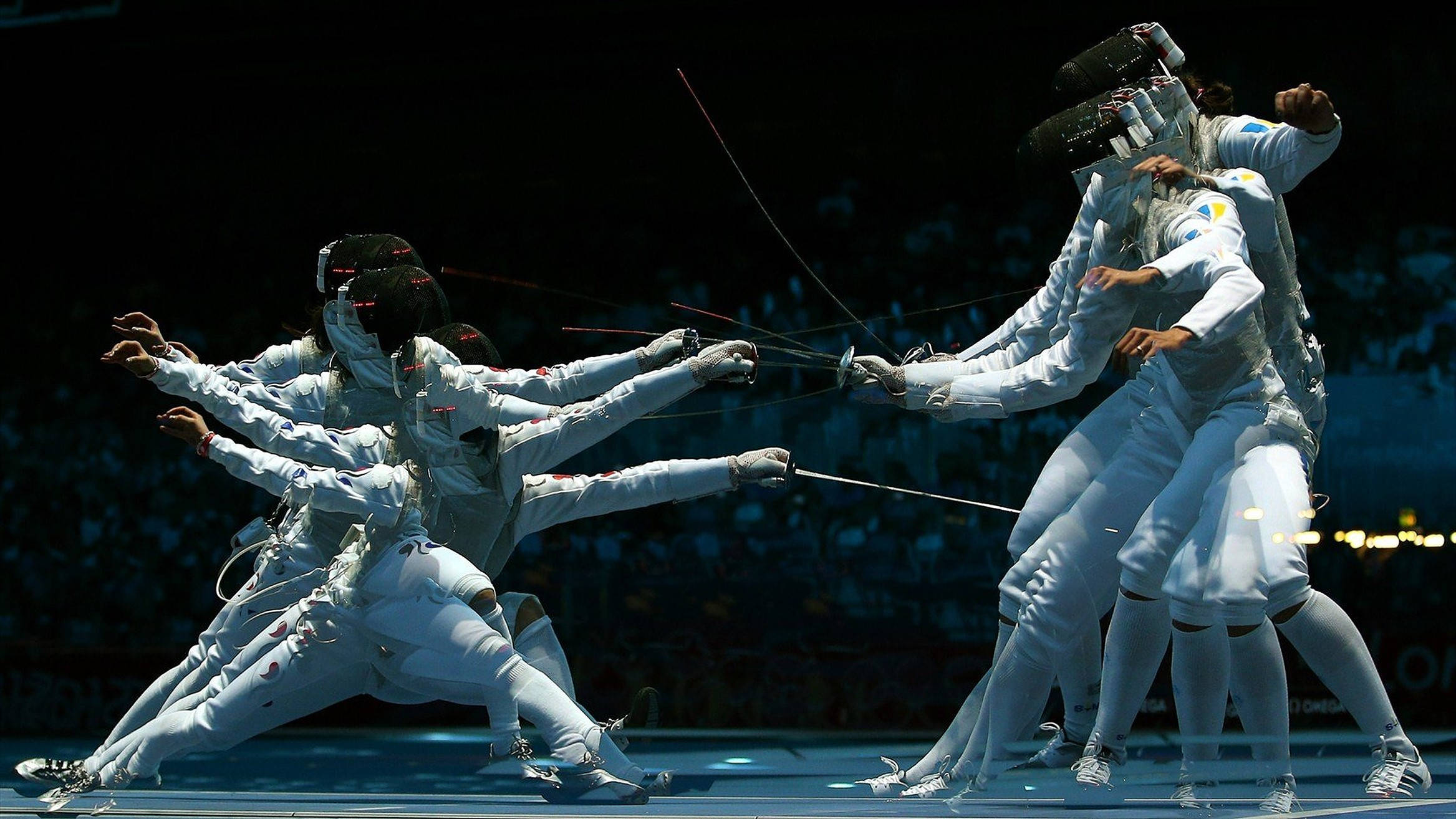 Fencing 桌布 壁紙 — 身穿白色裝備的劍擊手在明亮的場館燈光下，以黑暗的人群為背景，揮劍交鋒。