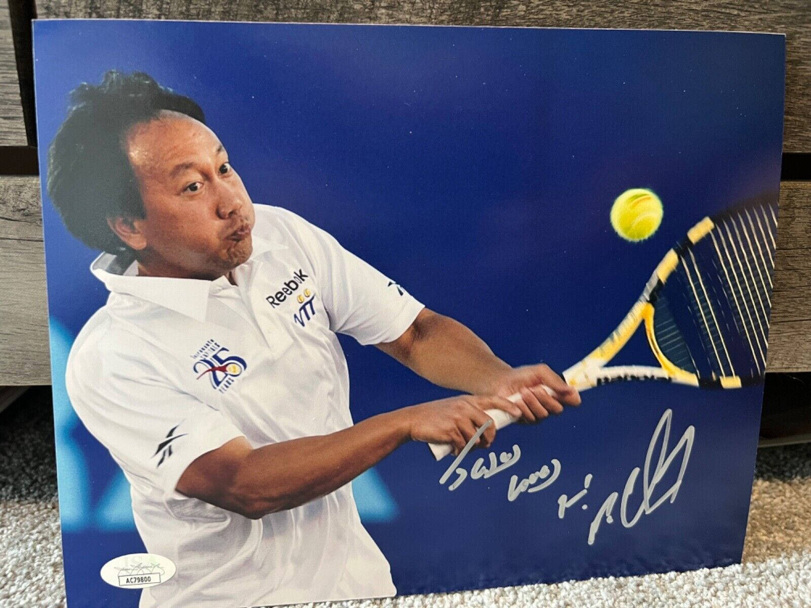Tennis 桌布 壁紙 — 身穿白色襯衫的網球運動員在藍色背景上揮拍擊打黃色球，附有簽名。