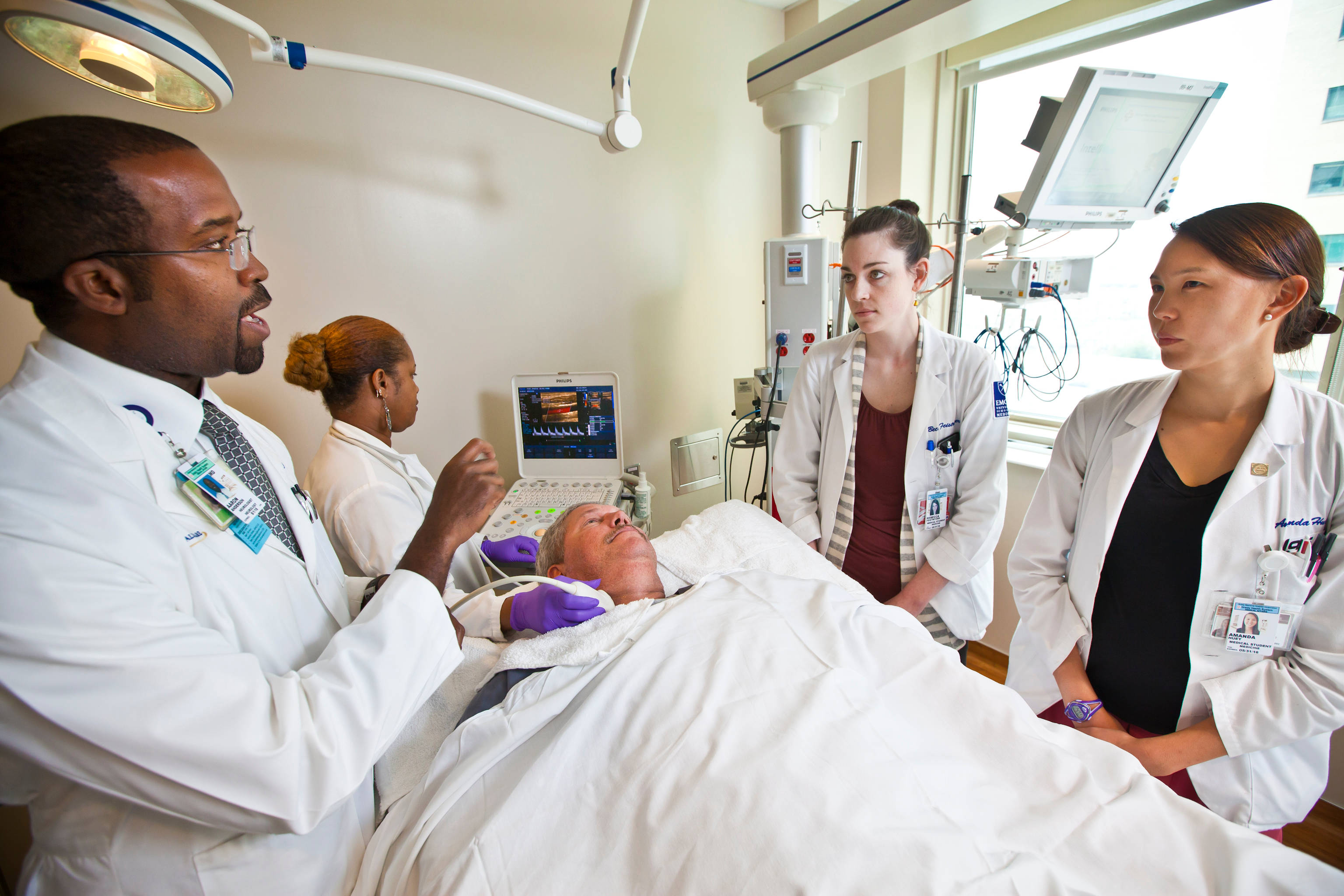 Hospital 桌布 壁紙 — 身穿白袍的醫療團隊圍繞著病床上帶有監視器和靜脈注射設備的病人。