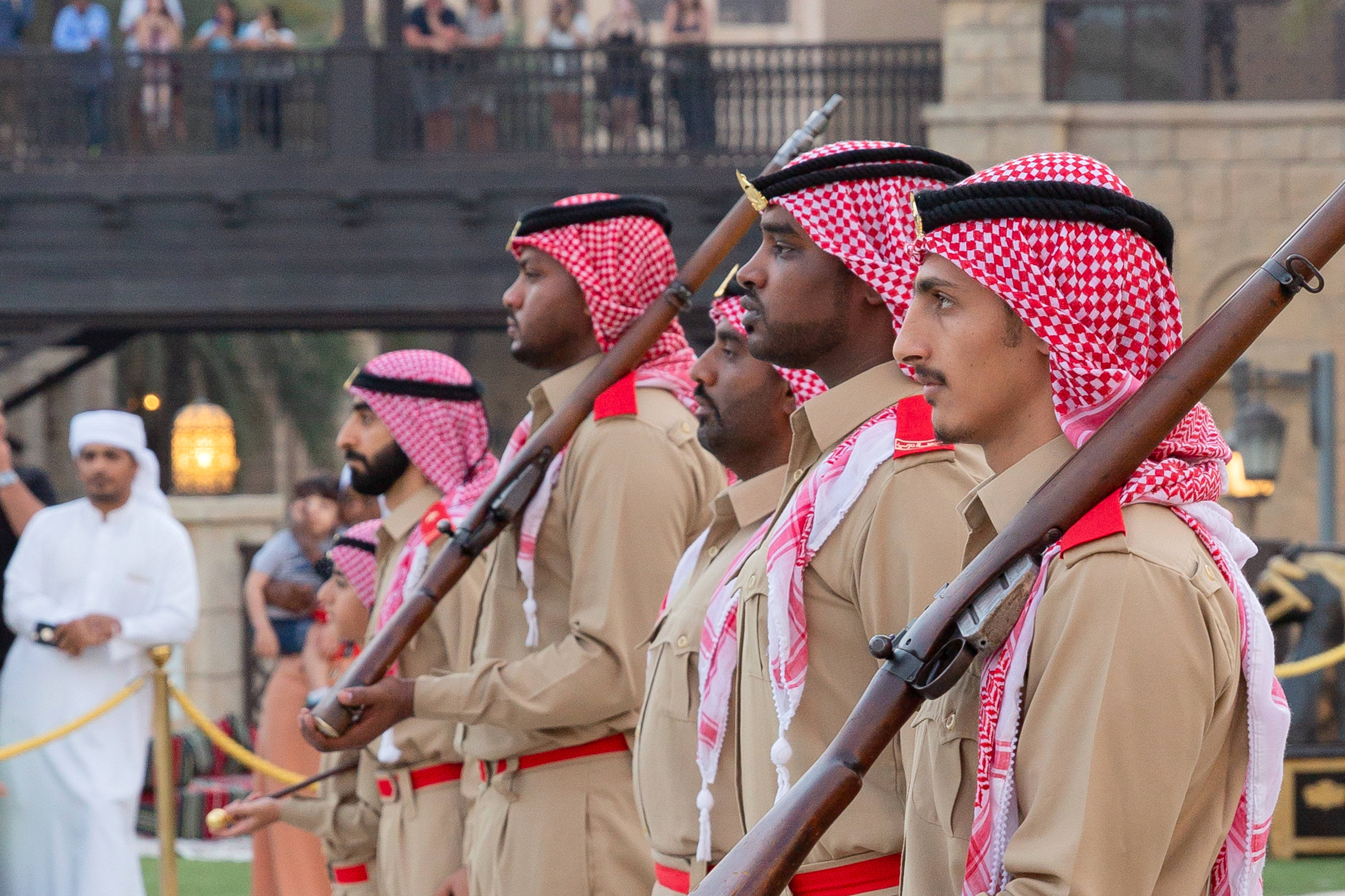 Ramadan 桌布 壁紙 — 身穿米色制服和紅色格子頭巾的士兵在儀式遊行中精確地排列成隊形，手持步槍。