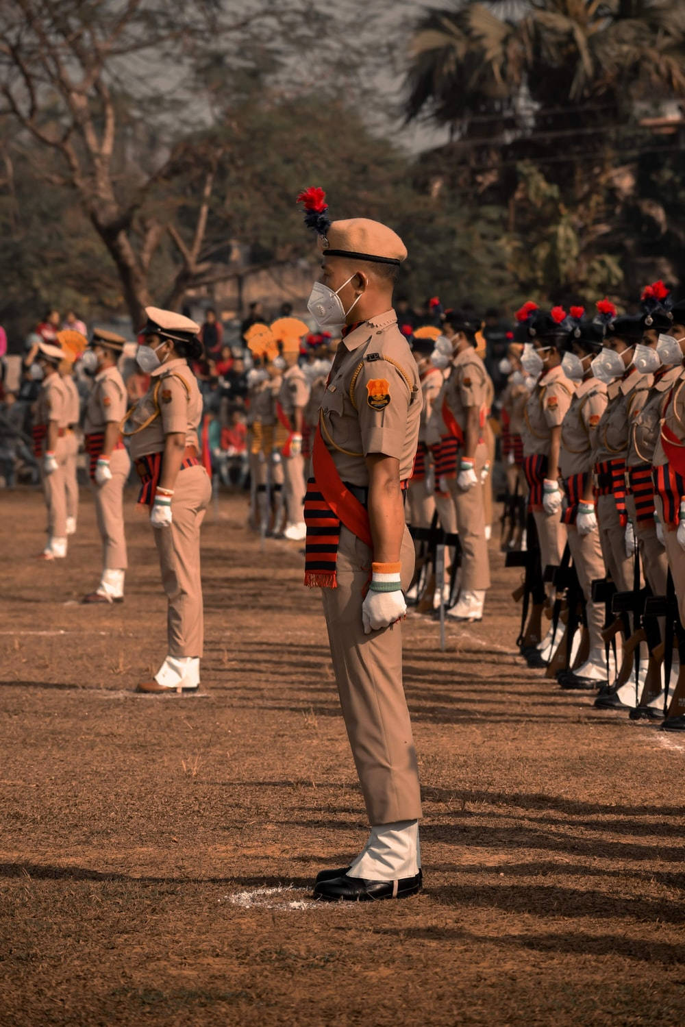 Indian 桌布 壁紙 — 身穿米色制服的士兵在乾燥的土地上，在溫暖的陽光下，以棕櫚樹為背景，精確地排列成行，立正站著。