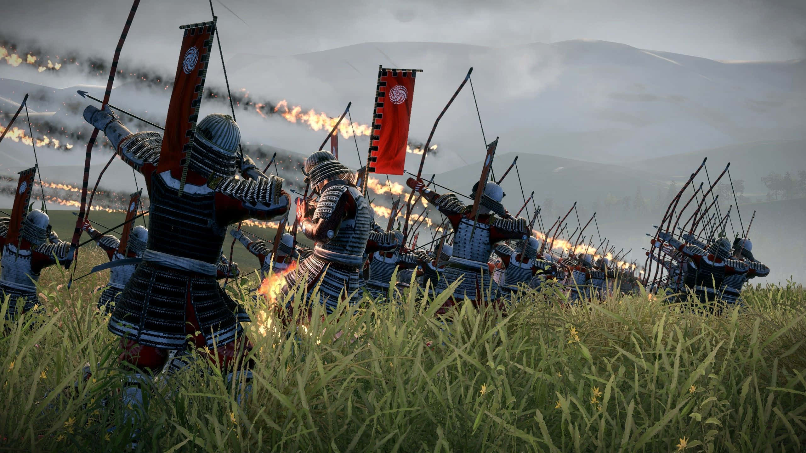 Shogun 桌布 壁紙 — 身穿精細盔甲的武士弓箭手在陰天之下，從草地射箭，伴有煙霧和遠處的火焰。