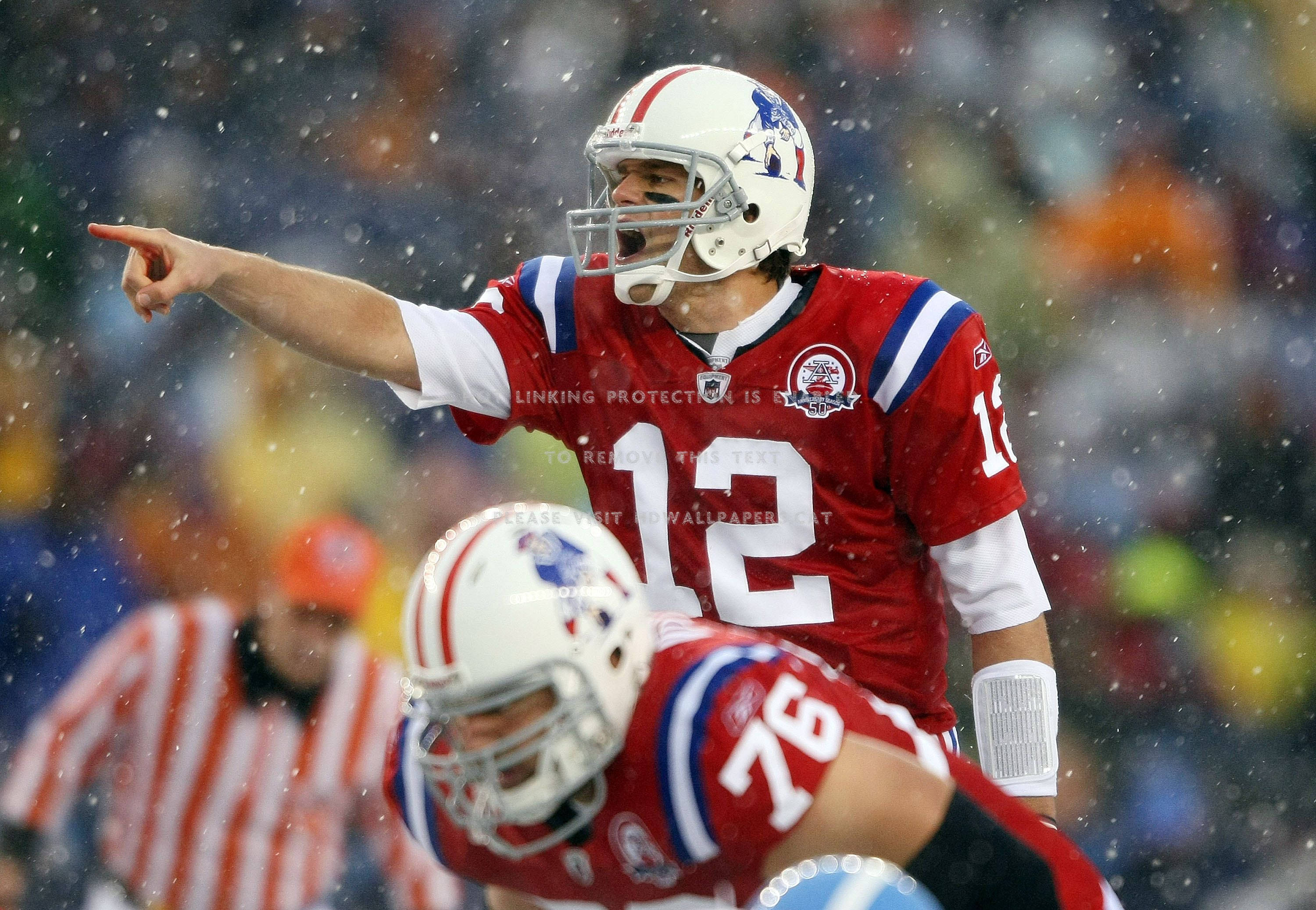 Tom Brady 桌布 壁紙 — 身穿紅色12號球衣的美式足球四分衛在雪地比賽中激烈地向前指，76號隊友在旁觀看。