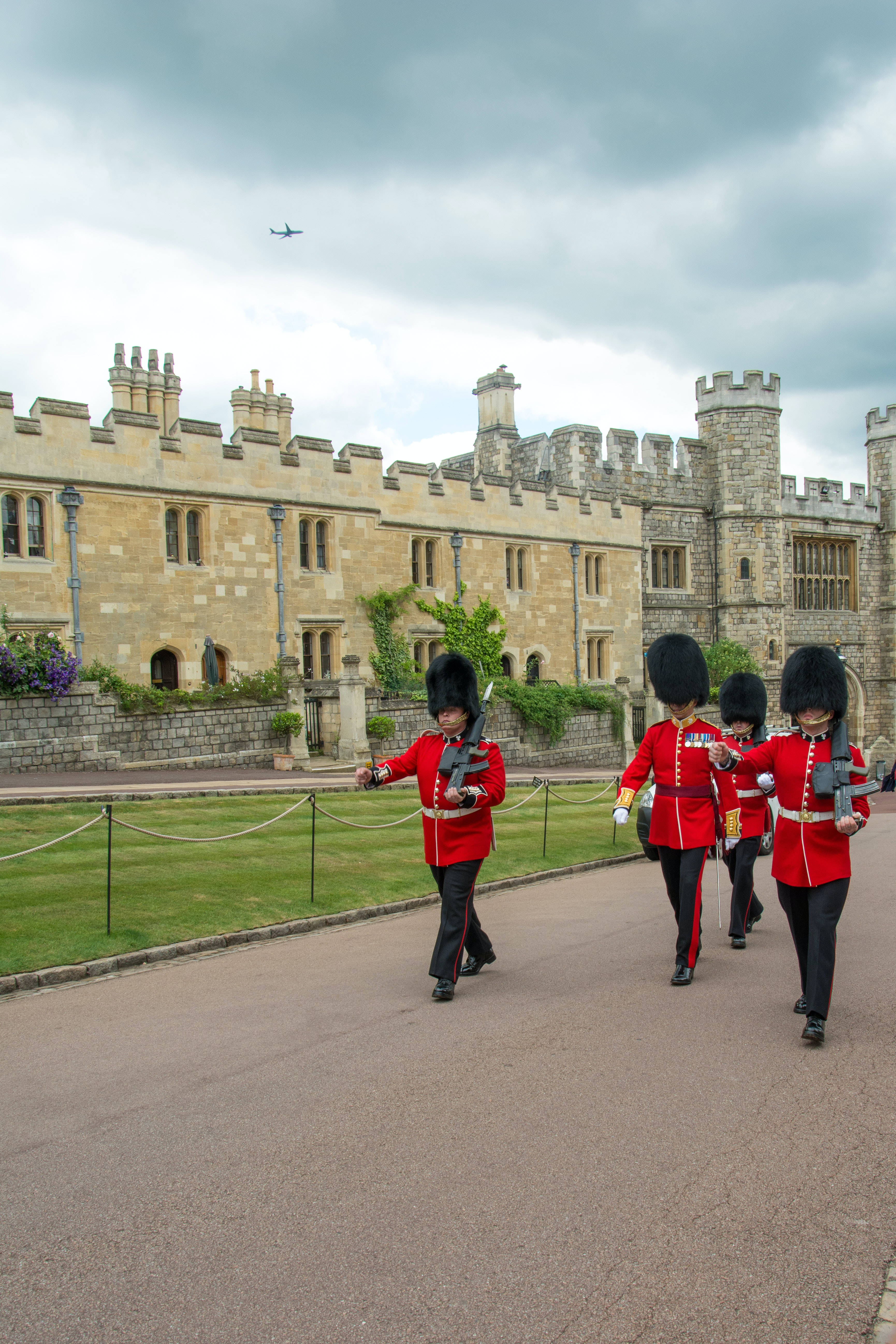 England 桌布 壁紙 — 身穿紅色制服、頭戴黑色高帽的士兵，在陰天下列隊走過一座歷史悠久的石城堡。