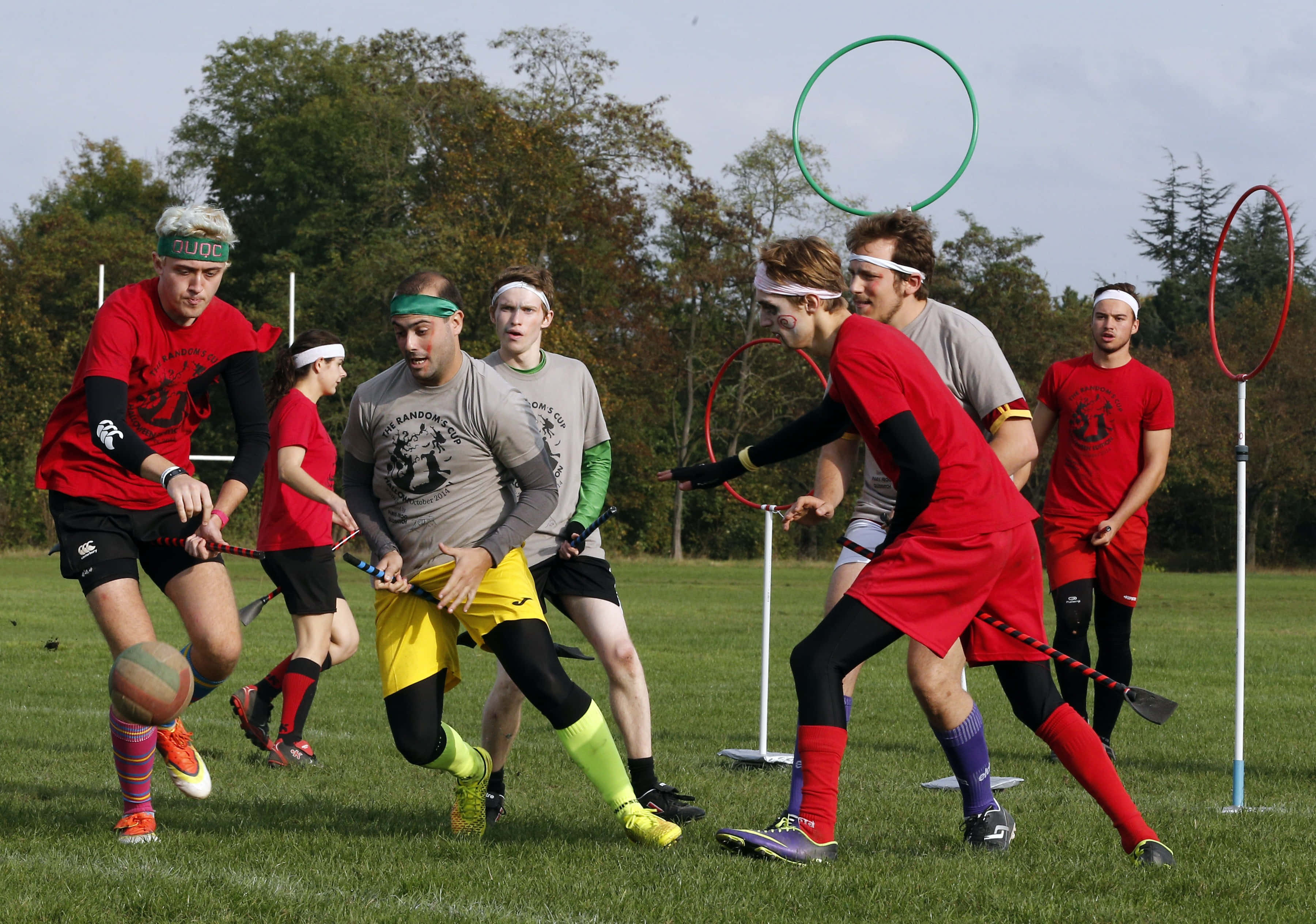 Quidditch 桌布 壁紙 — 身穿紅色和灰色球衣的球員在草地上進行激烈的曲棍球比賽，球門為圓環形。