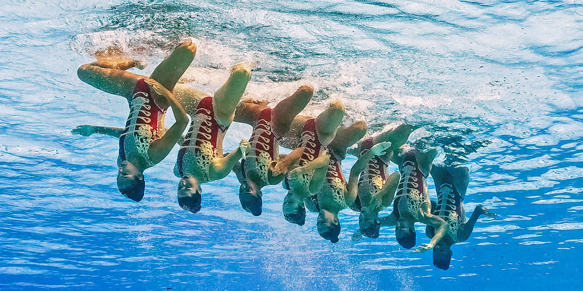 Swimming 桌布 壁紙 — 身穿紅色和白色服裝的韻律泳運動員在清澈的藍色泳池水中表演精確的水下隊形。