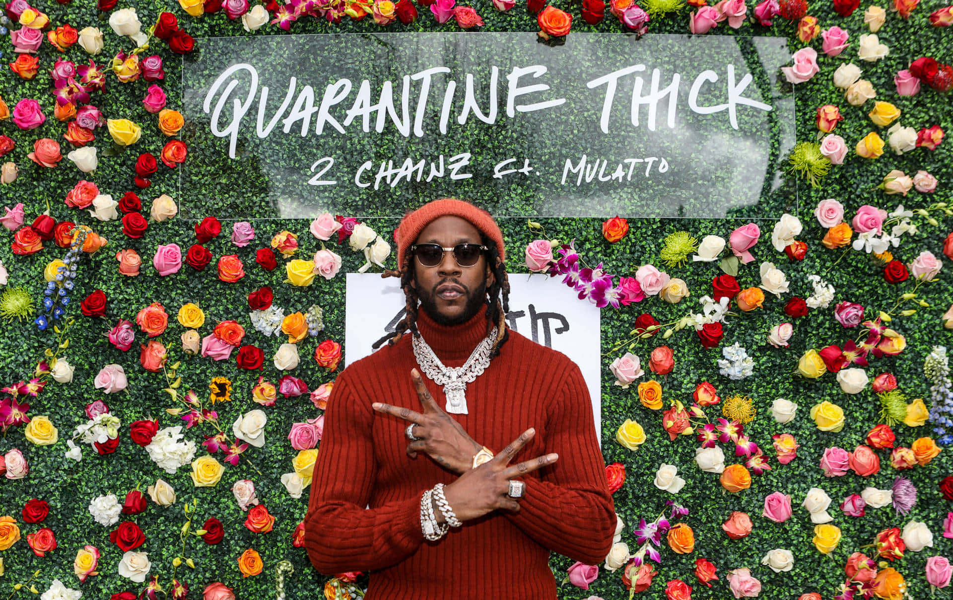 2 Chainz 桌布 壁紙 — 身穿紅色毛衣和毛帽的男子自信地站在充滿活力的花卉牆前，牆上寫有 'QUARANTINE THICK' 字樣。