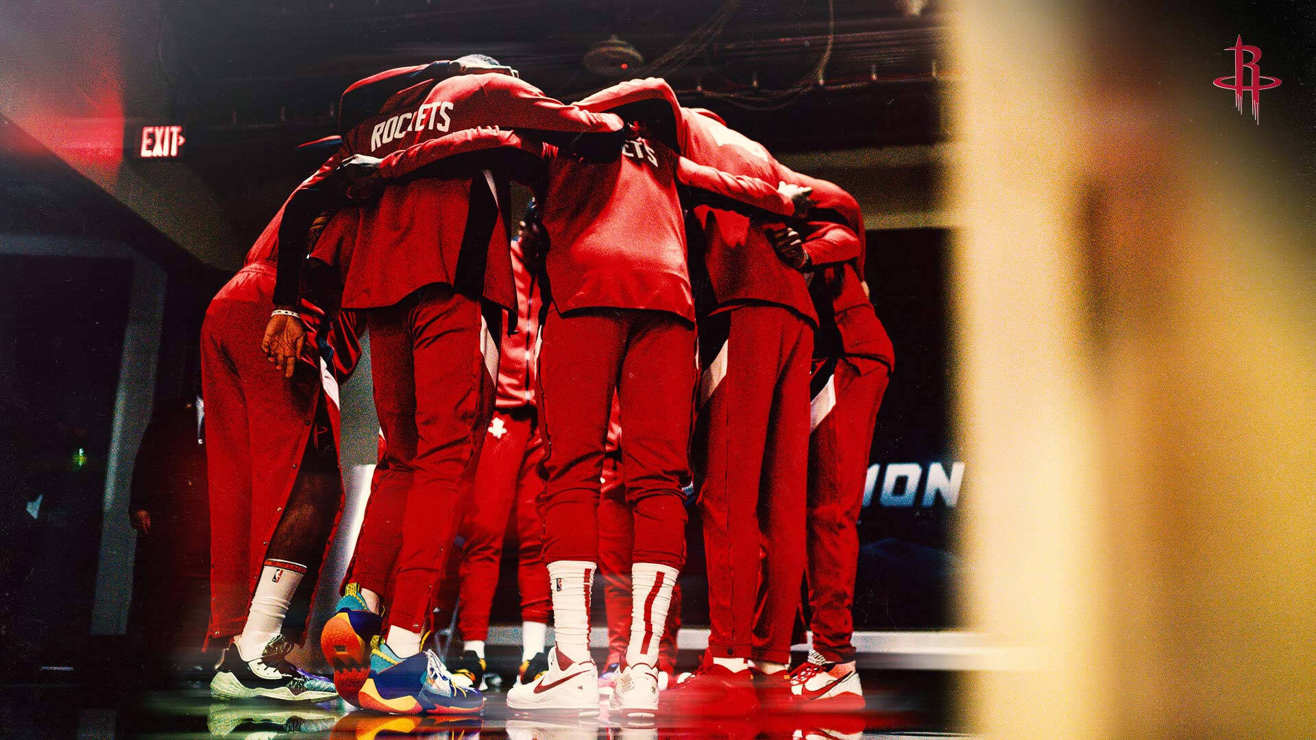Houston Rockets 桌布 壁紙 — 身穿紅色火箭隊球衣的籃球運動員在體育館燈光下，在光滑的球場上緊密圍攏。