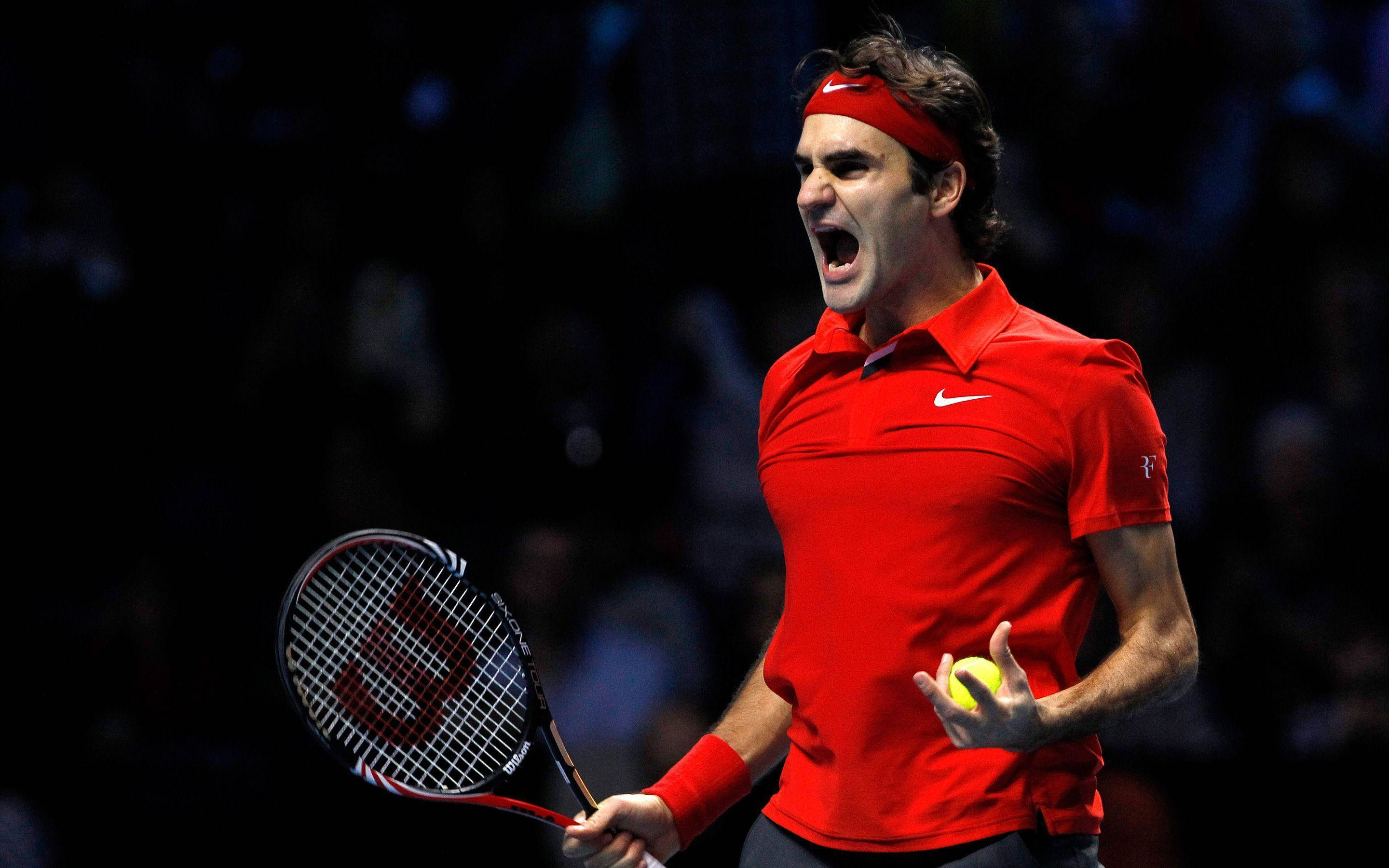 roger 桌布 壁紙 — 身穿紅色球衣和頭帶的網球選手在場館燈光下高舉球拍和球，發出勝利的吼叫。