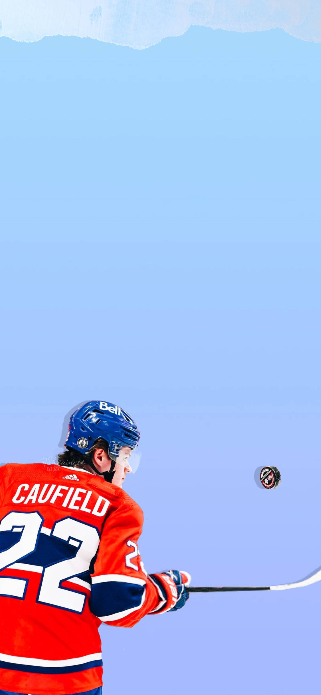 Cole Caufield 桌布 壁紙 — 身穿紅色球衣的冰球運動員Caufield準備在晴朗藍天和遠山背景下射門。