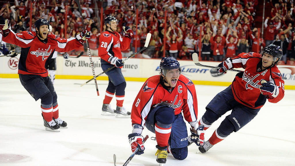 Washington Capitals 桌布 壁紙 — 身穿紅色球衣的曲棍球運動員在冰上瘋狂慶祝，身後身穿紅衣的歡呼球迷擠滿了場館。