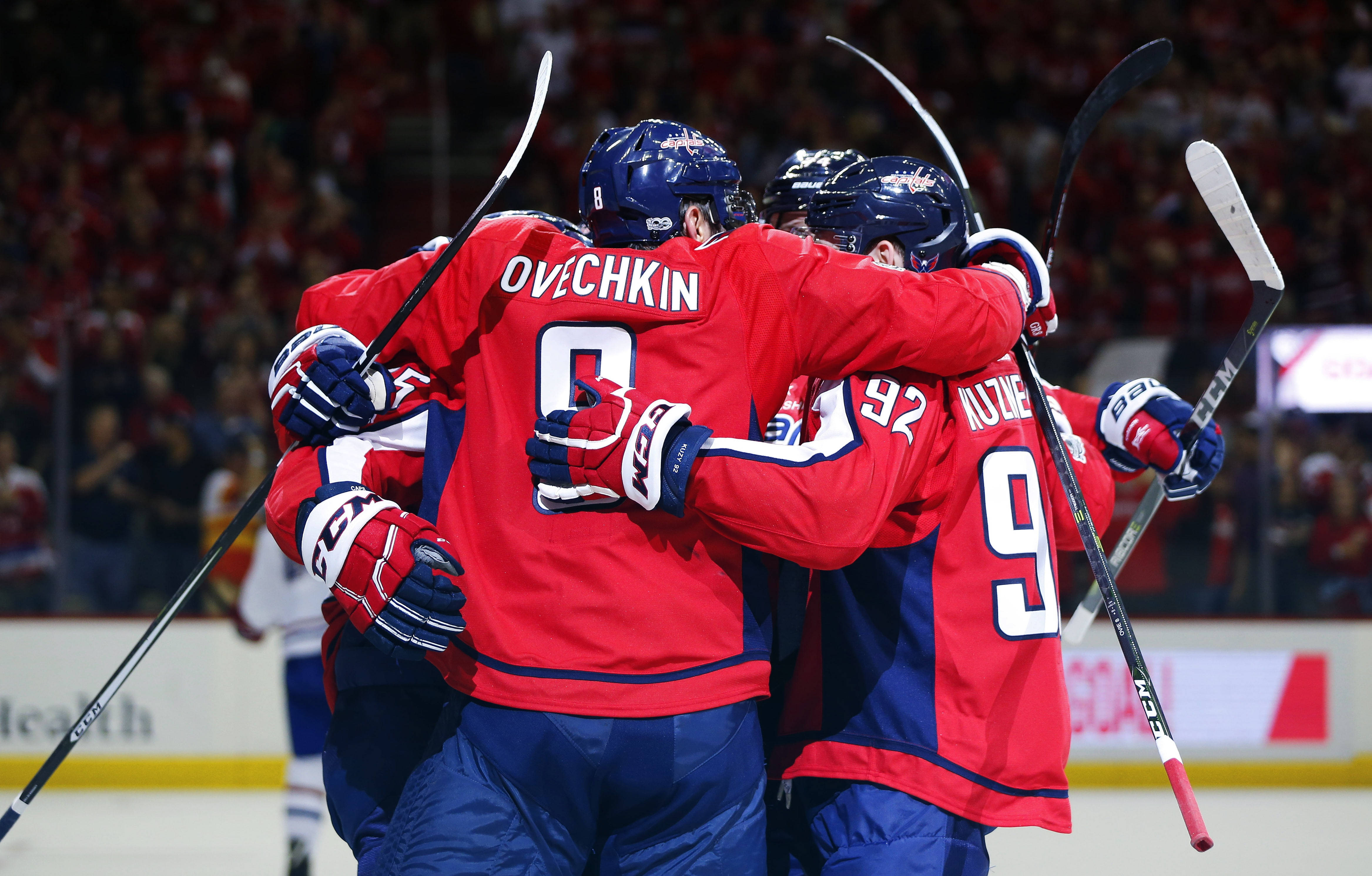 hockey 桌布 壁紙 — 身穿紅色球衣的曲棍球運動員在明亮的場館燈光下，在冰上緊密地聚在一起慶祝進球。