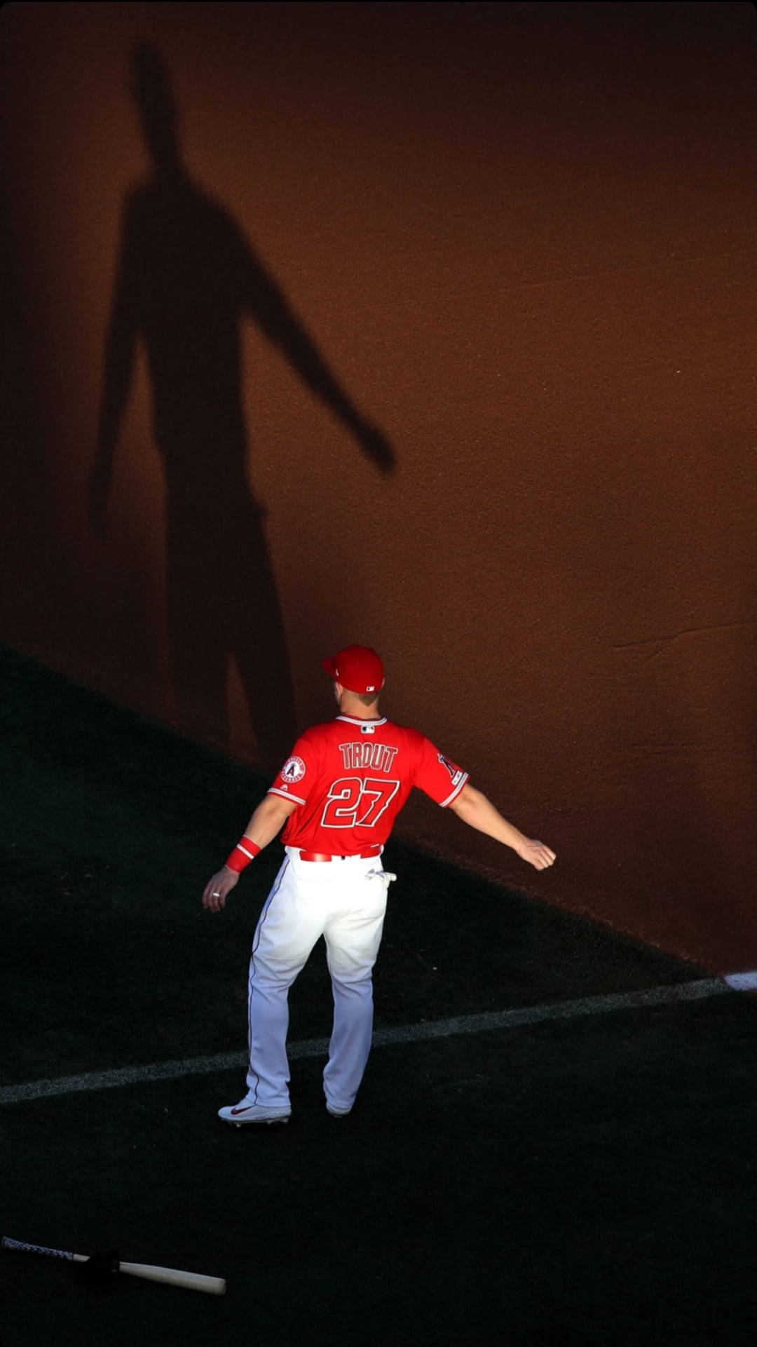 Mike Trout 桌布 壁紙 — 身穿紅色球衣的棒球運動員Mike Trout在體育場燈光下，在棕色牆壁上投下長長的戲劇性陰影。