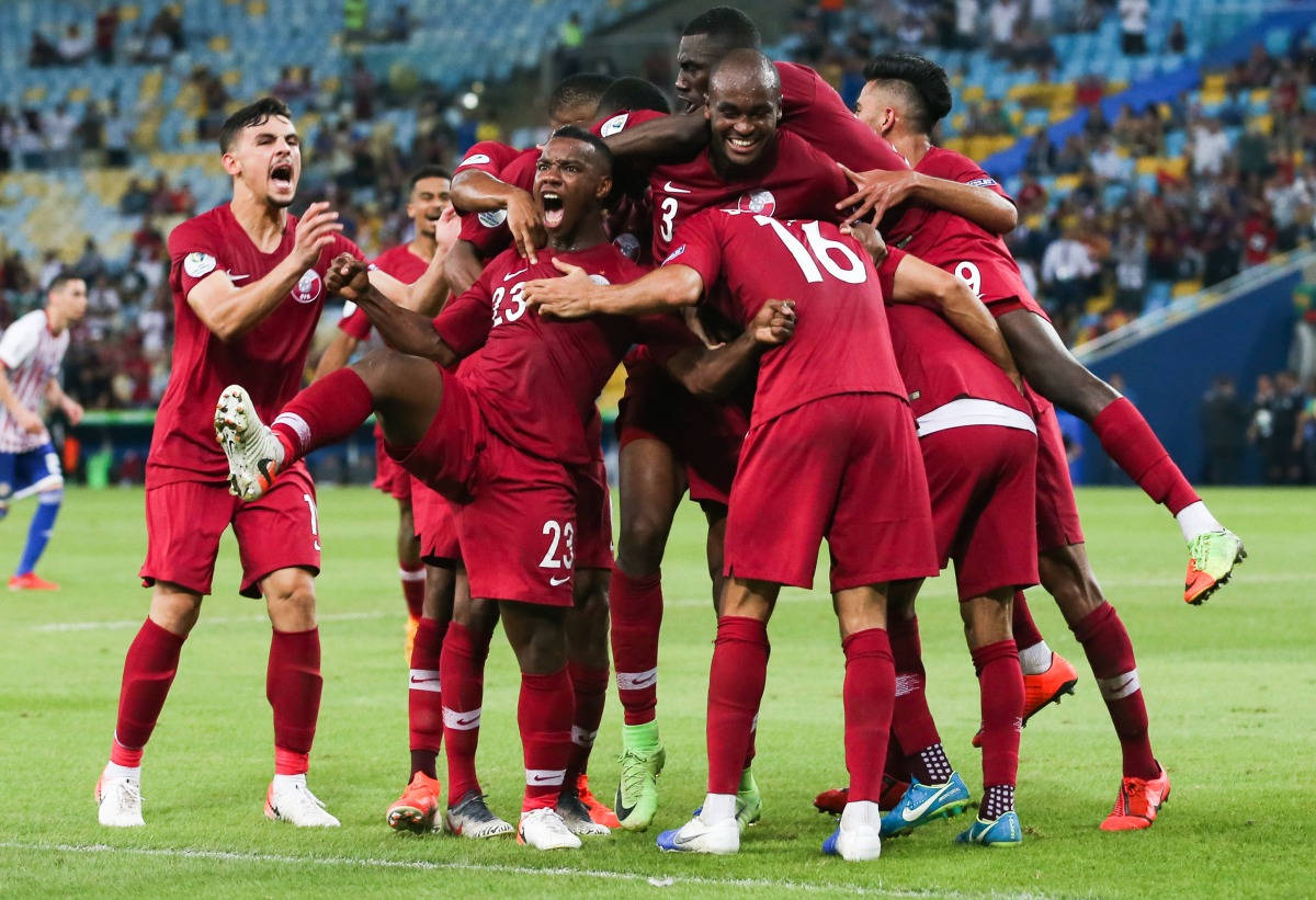 Qatar 桌布 壁紙 — 身穿紅色球衣的足球員在球場燈光下，於充滿活力的綠色草地上瘋狂慶祝進球，互相擁抱。