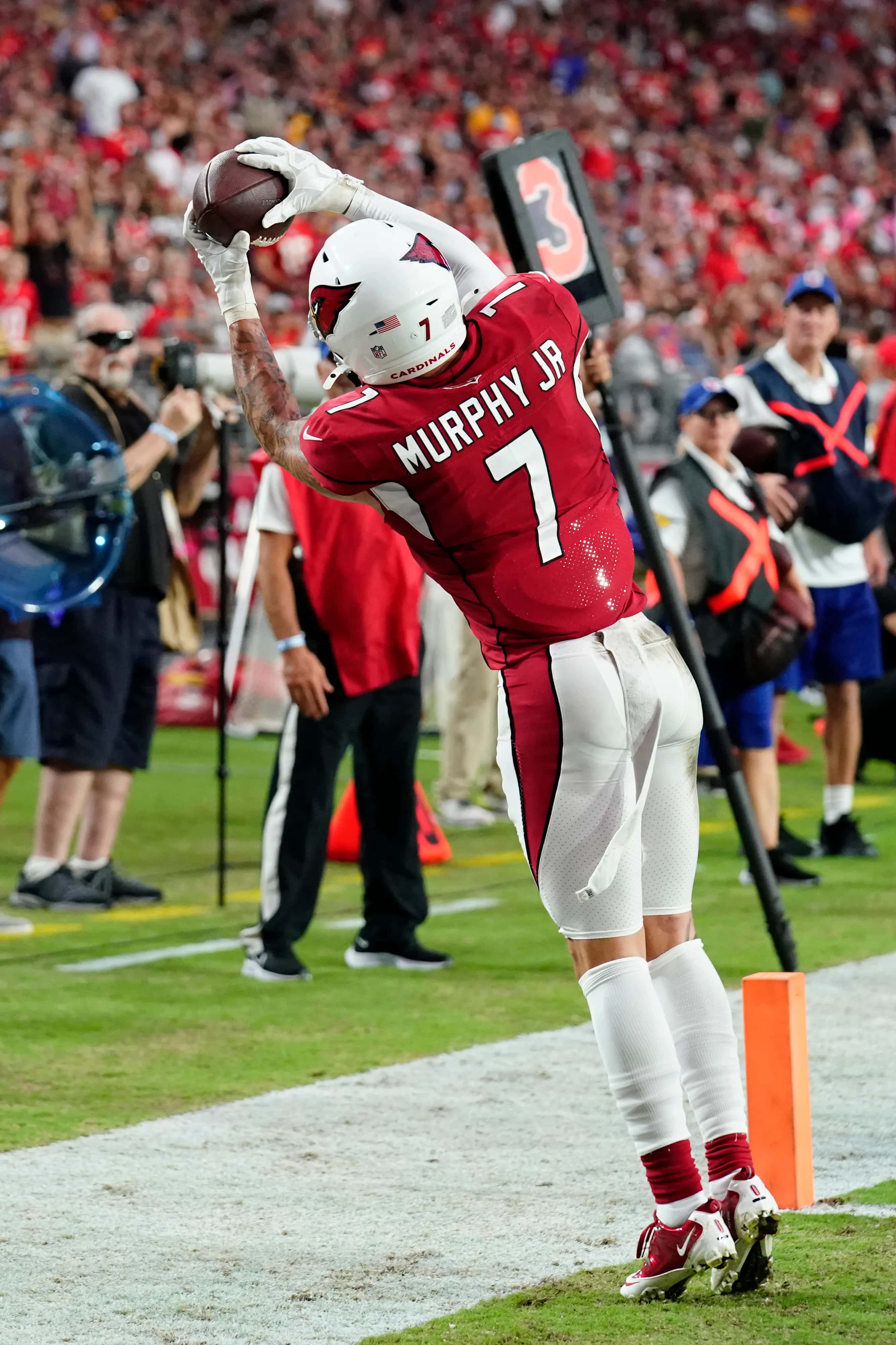 Byron Murphy 桌布 壁紙 — 身穿紅色球衣的足球運動員Murphy Jr在背景有觀眾的情況下，在端區附近接住達陣。