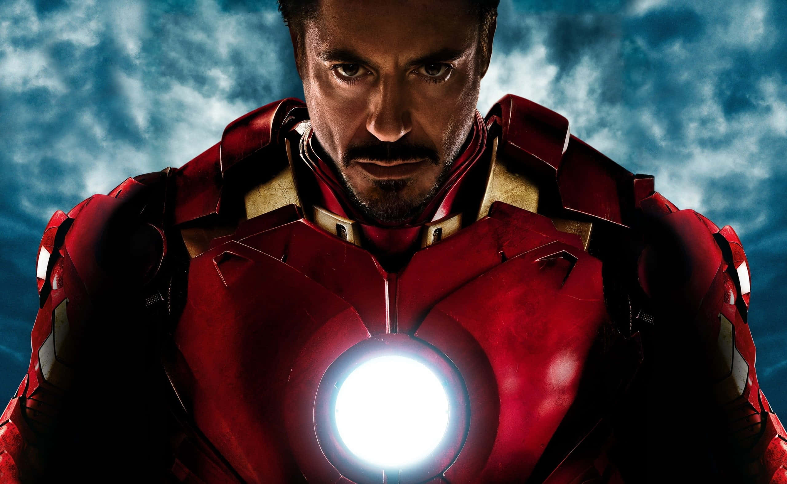 Superhero Movies 桌布 壁紙 — 身穿紅色裝甲的鋼鐵人，在暴風雨藍天下，帶著發光的弧形反應爐，凝視著。