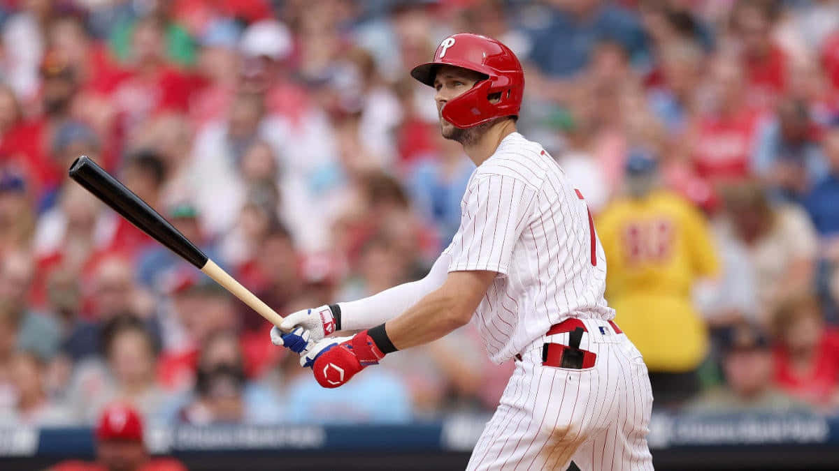 Trea Turner Phillies 桌布 壁紙 — 身穿紅色頭盔和細條紋球衣的棒球選手正在揮棒，背景是模糊的人群。
