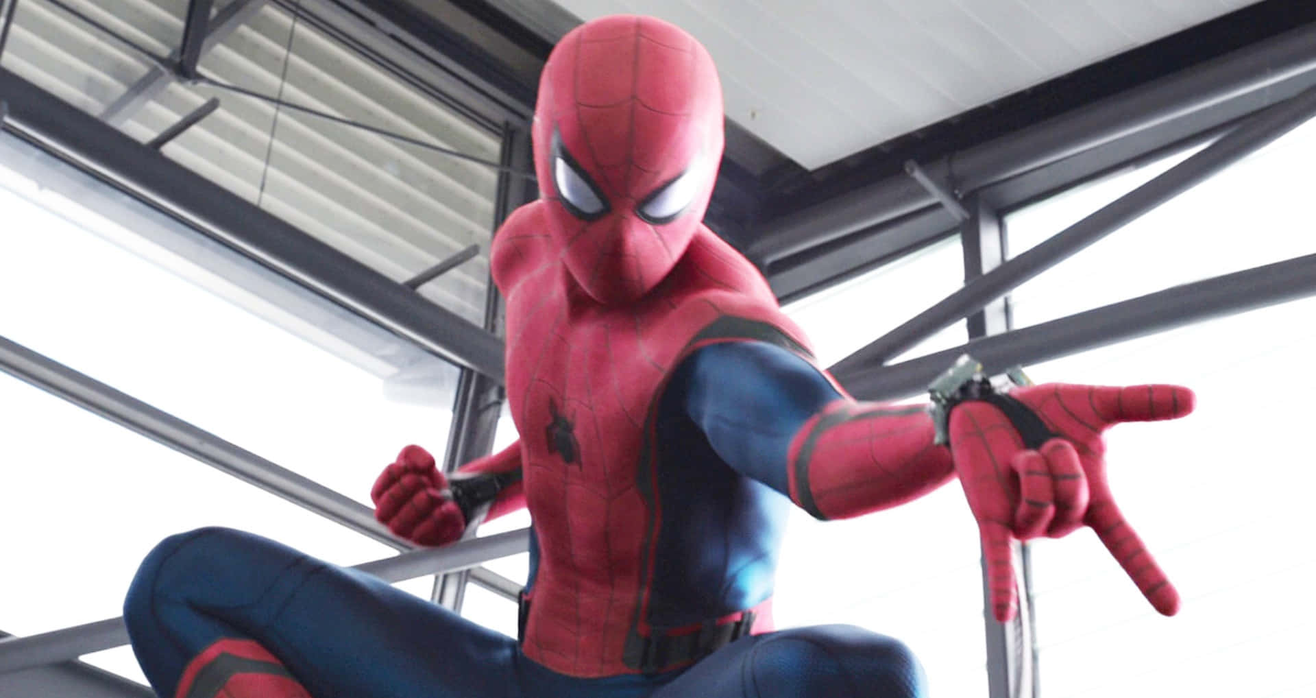 Spider-man Web Shooter 桌布 壁紙 — 身穿紅藍戰衣的蜘蛛人在明亮的日光下蹲在金屬橫樑上。