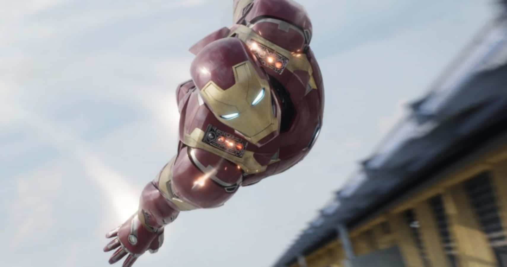 Vibranium Suit 桌布 壁紙 — 身穿紅金盔甲的鋼鐵人在陰天背景下於建築物旁懸浮在半空中。