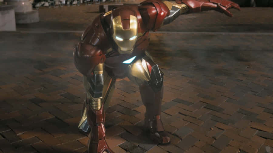 Iron Man Action Figures 桌布 壁紙 — 身穿紅金裝甲的鋼鐵人在昏暗的夜燈下蹲在濕漉漉的磚街上，眼睛和胸部弧形反應堆發光。
