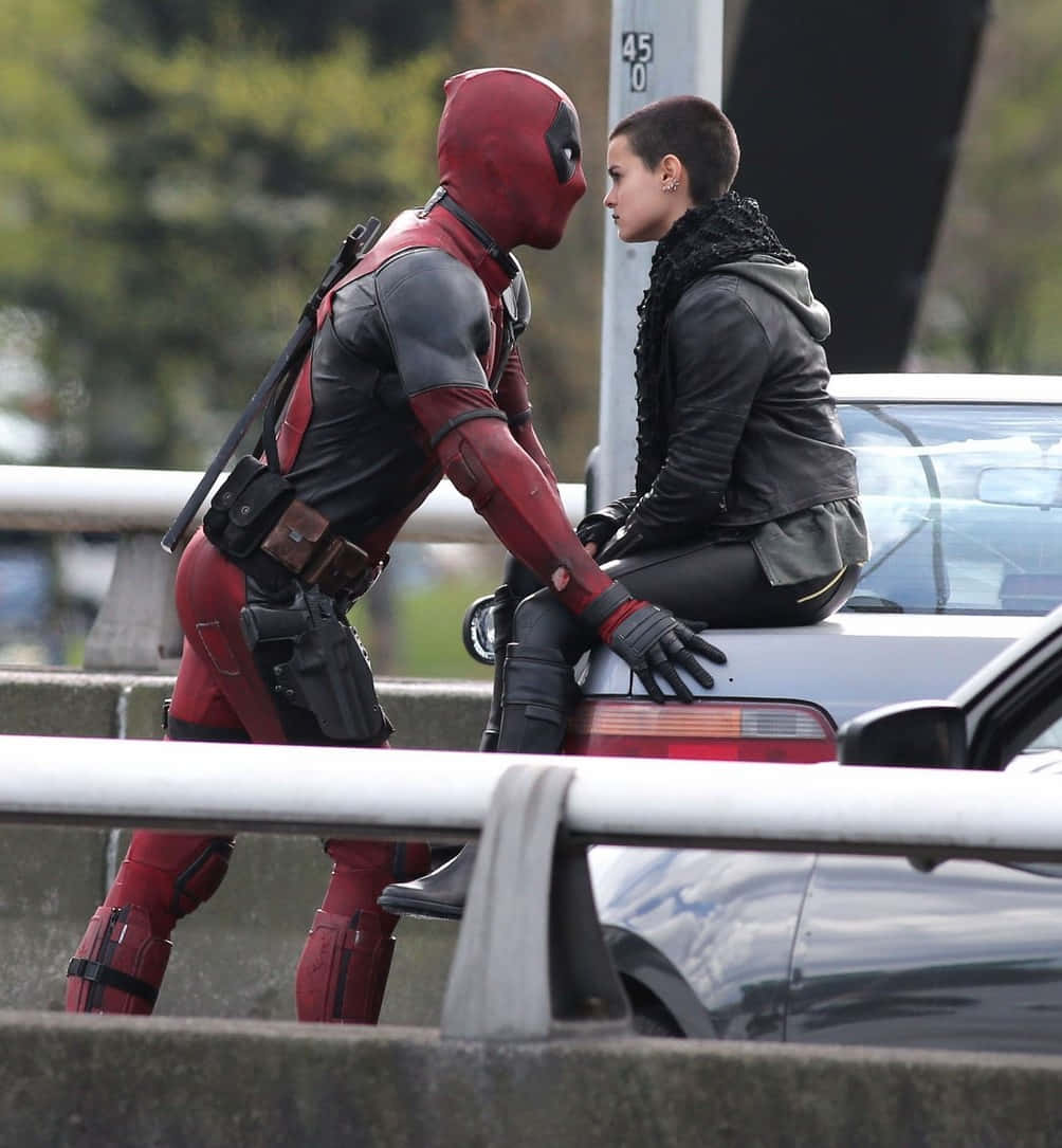 Deadpool And Negasonic Teenage Warhead 桌布 壁紙 — 身穿紅黑戰衣的死侍在天橋上靠著車頂，面向一位身穿黑色皮夾克的女子。