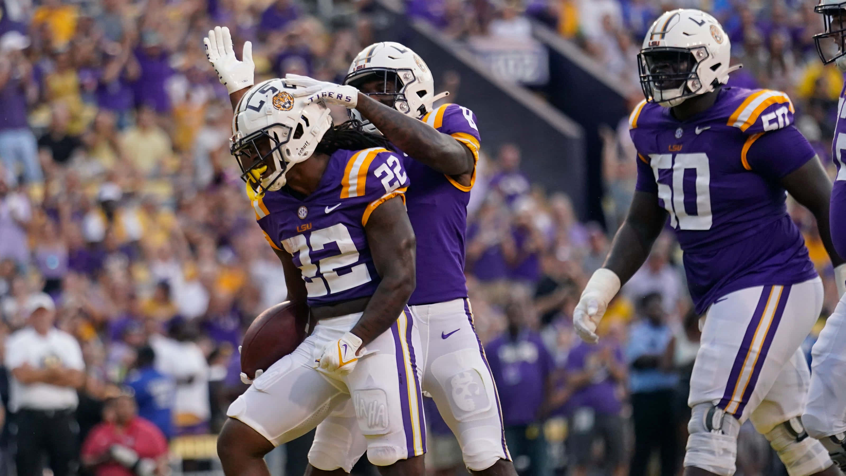 Lsu Football 桌布 壁紙 — 身穿紫色和金色球衣的LSU足球員在背景球迷的陪伴下慶祝達陣。